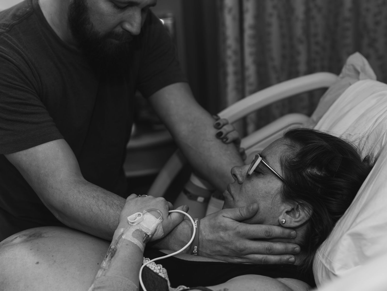 Black and white photo showing emotional moment between a couple in a hospital bed during labor and delivery.