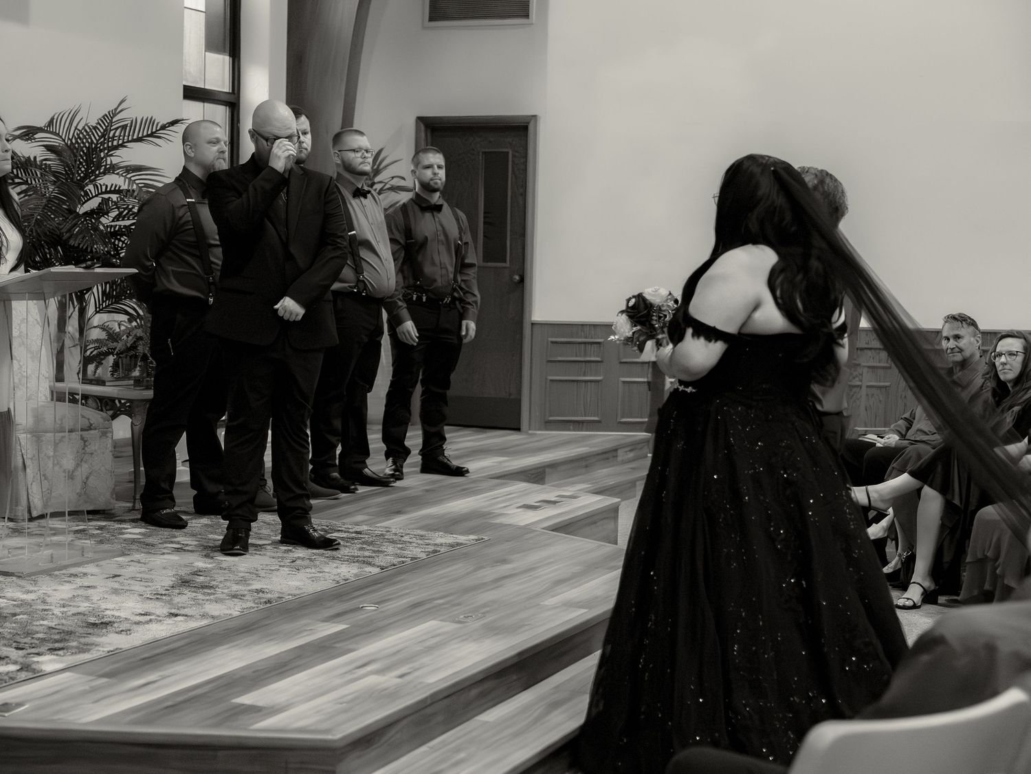 Black and white photo of a woman in a dark gown performing before a group of men in a modern indoor venue.