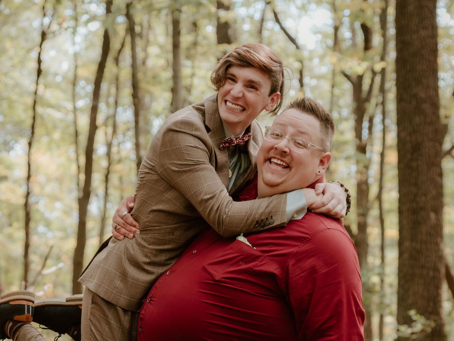 Joyful candid moment between wedding guests sharing a hug in the forest.