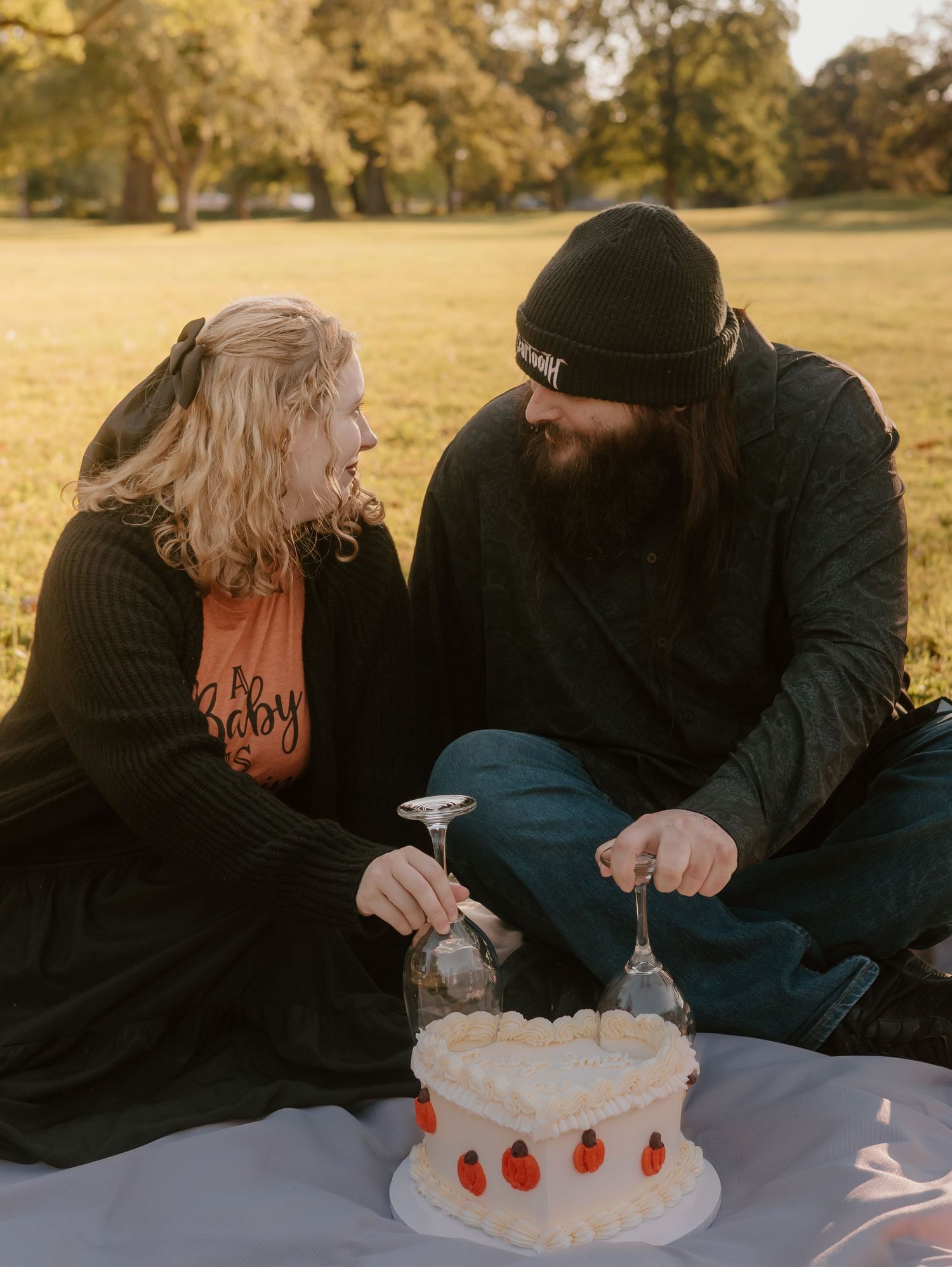 Couple blowing out candles together on a white frosted cake with red decorations.