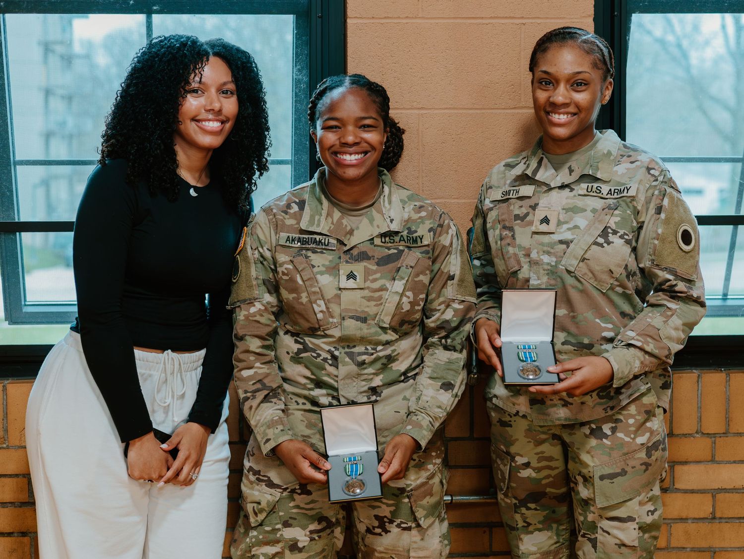 Three service members pose together for a photo while holding official documents at a military ceremony.