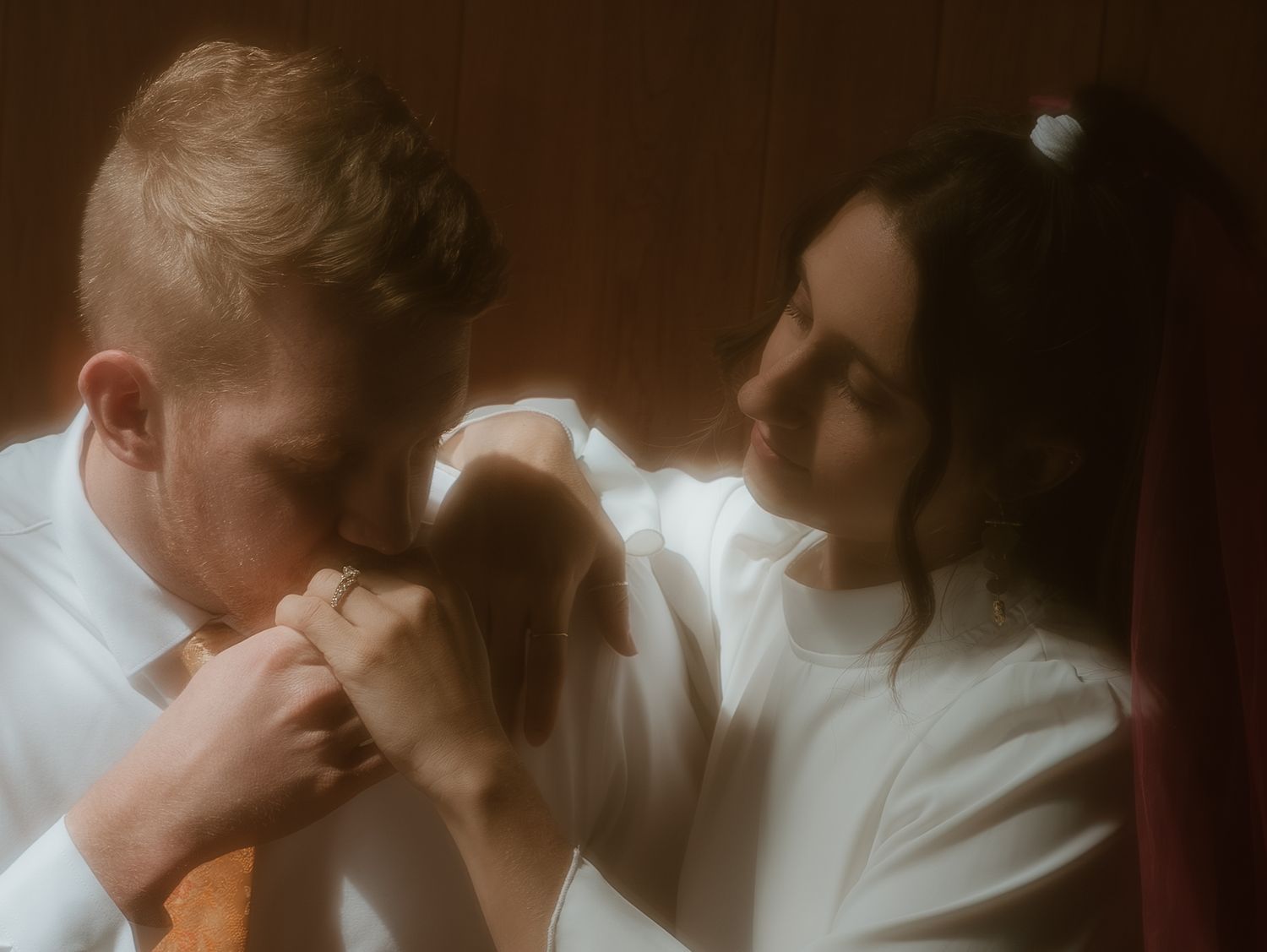 Two people in white attire embrace in an intimate vintage-style photograph with soft, dreamy lighting effects.