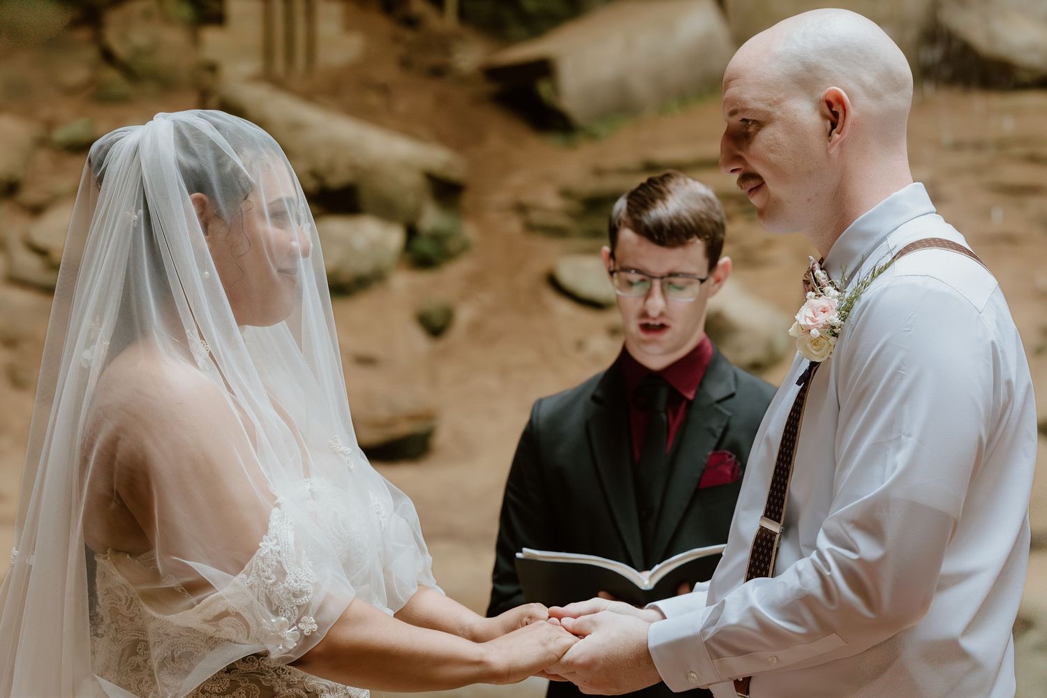 A romantic wedding ceremony moment captured in a rustic outdoor setting with stone walls in the background.