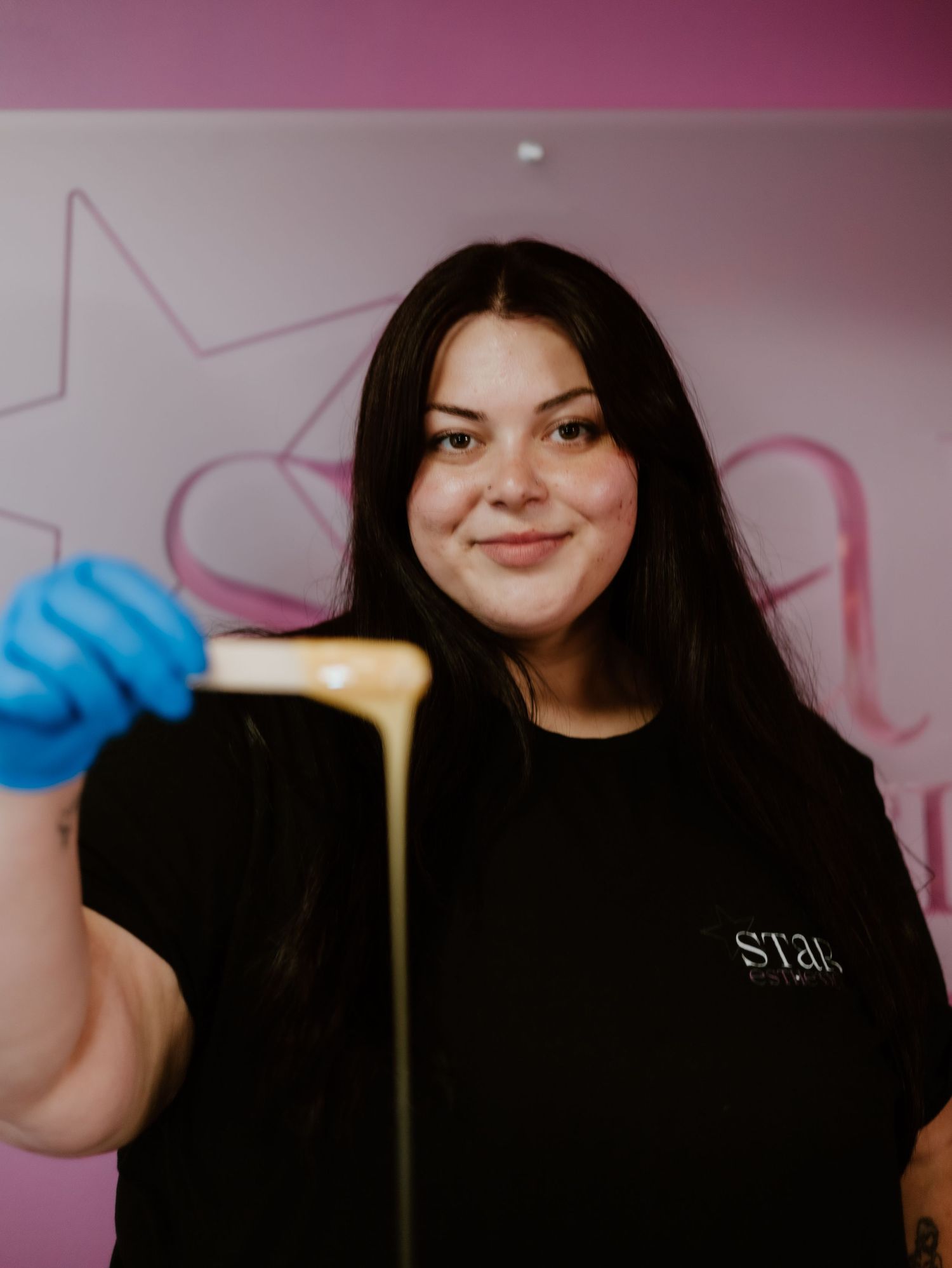 Someone wearing blue gloves stretches melted cheese in front of a pink wall with star decorations.