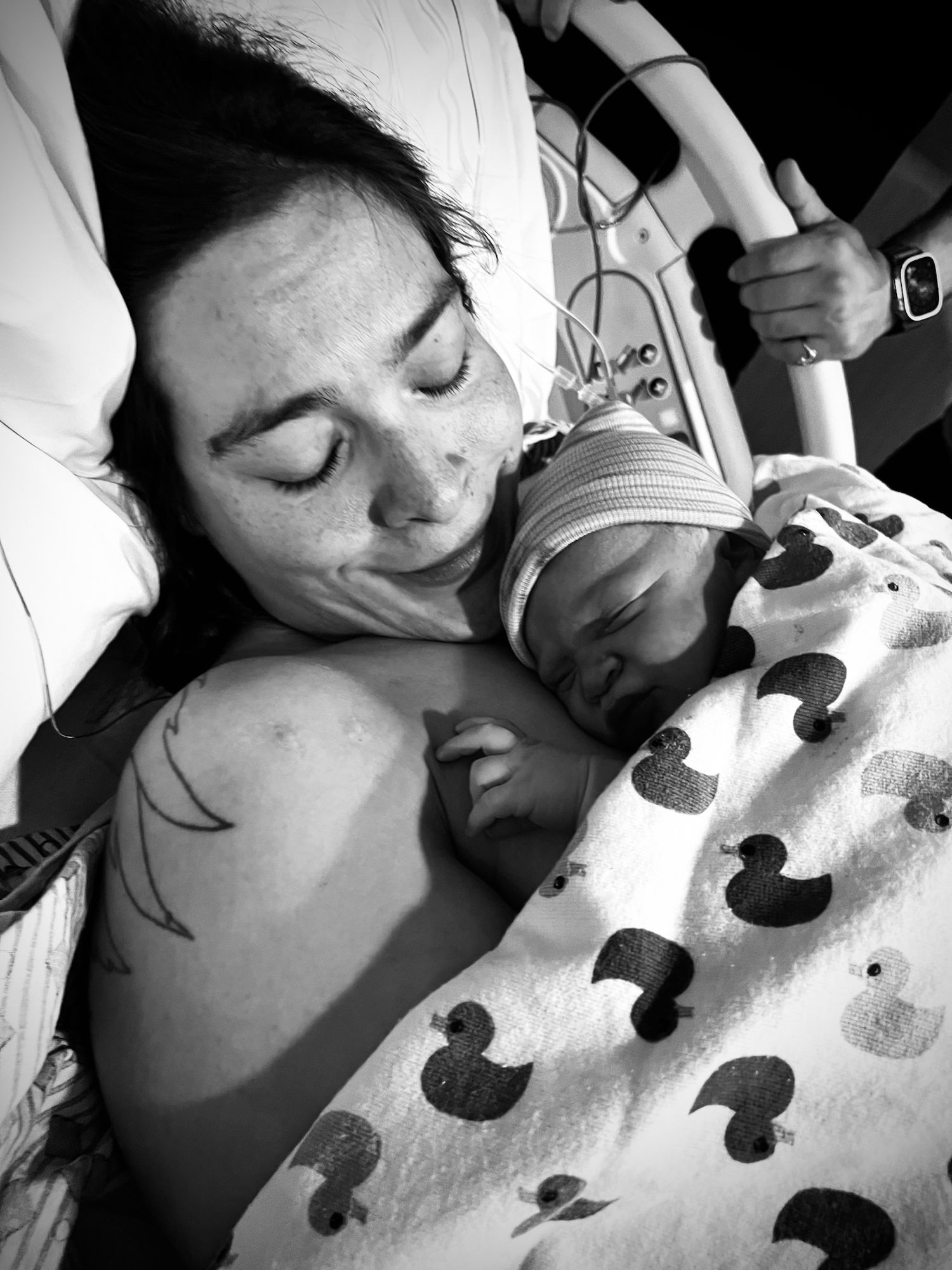 A tender moment captured in black and white as a newborn rests on a duck-patterned hospital blanket.