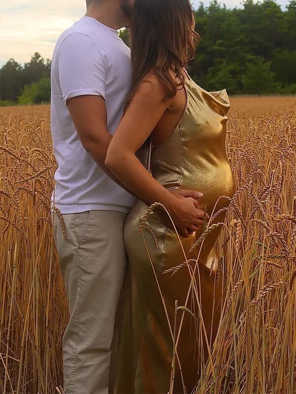 Couple embraces in a golden wheat field at sunset wearing white and gold clothing.
