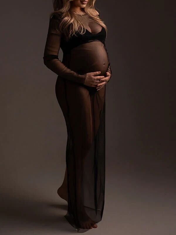 A silhouetted pregnant figure in a sheer dark gown poses against a moody brown backdrop for a maternity photoshoot.