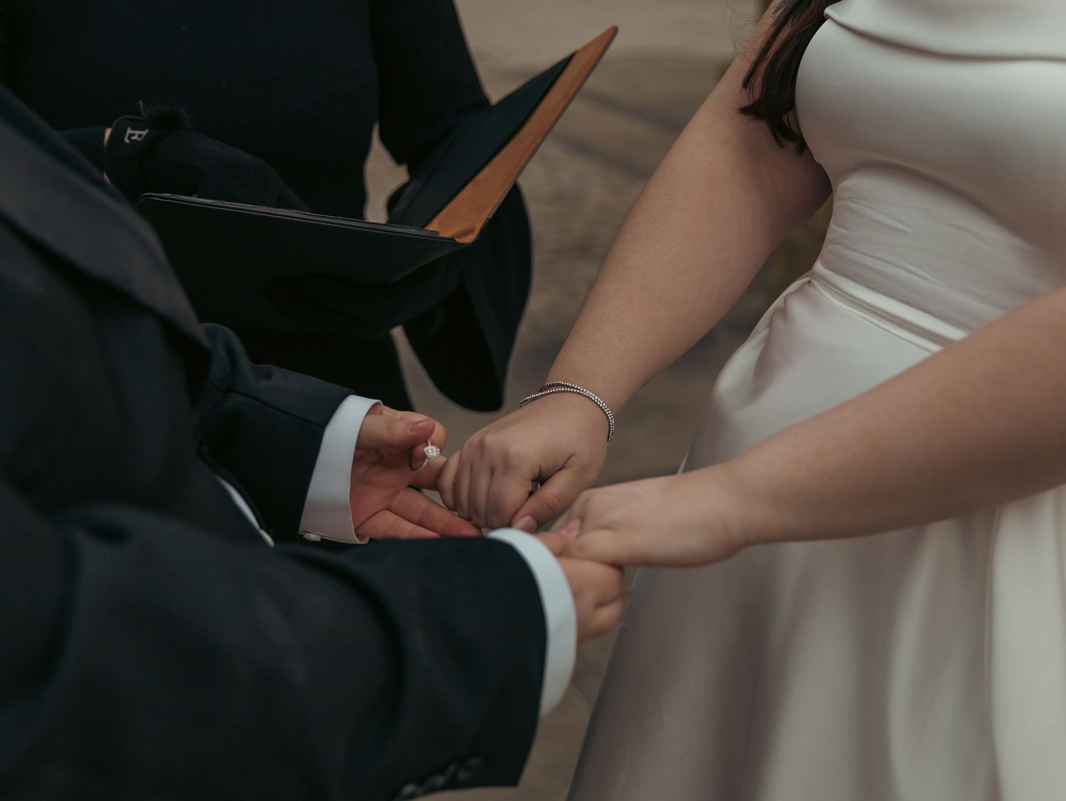 Hands exchanging rings during wedding ceremony against white dress background.