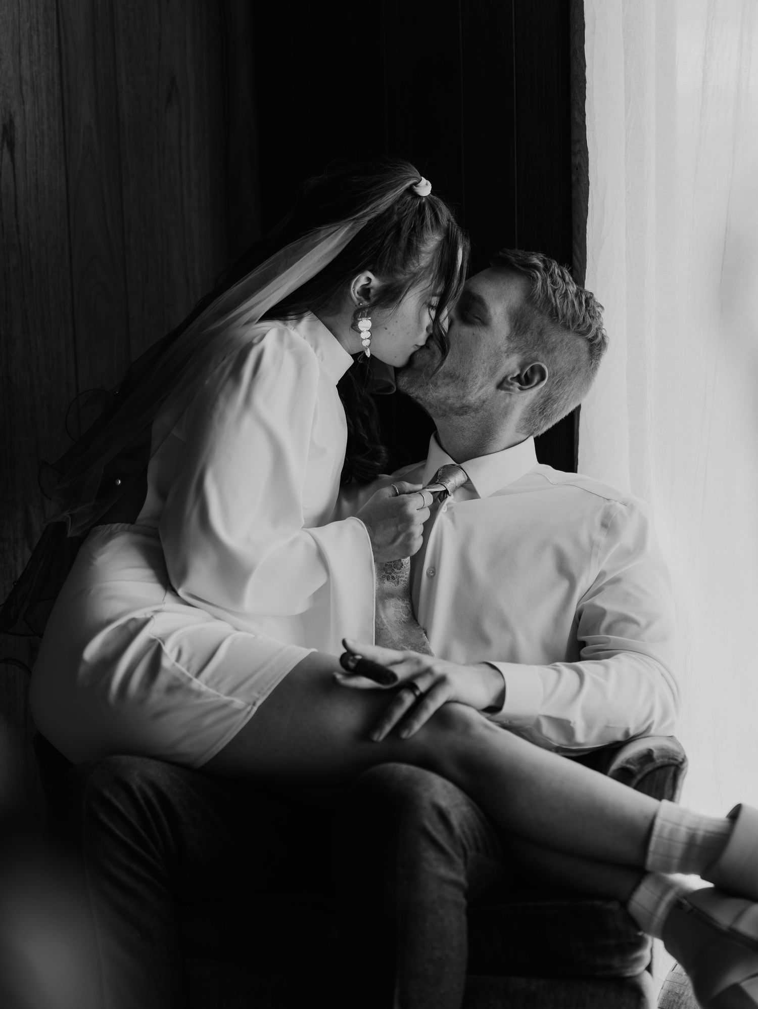 Intimate black and white wedding photo of couple sharing romantic moment near window.