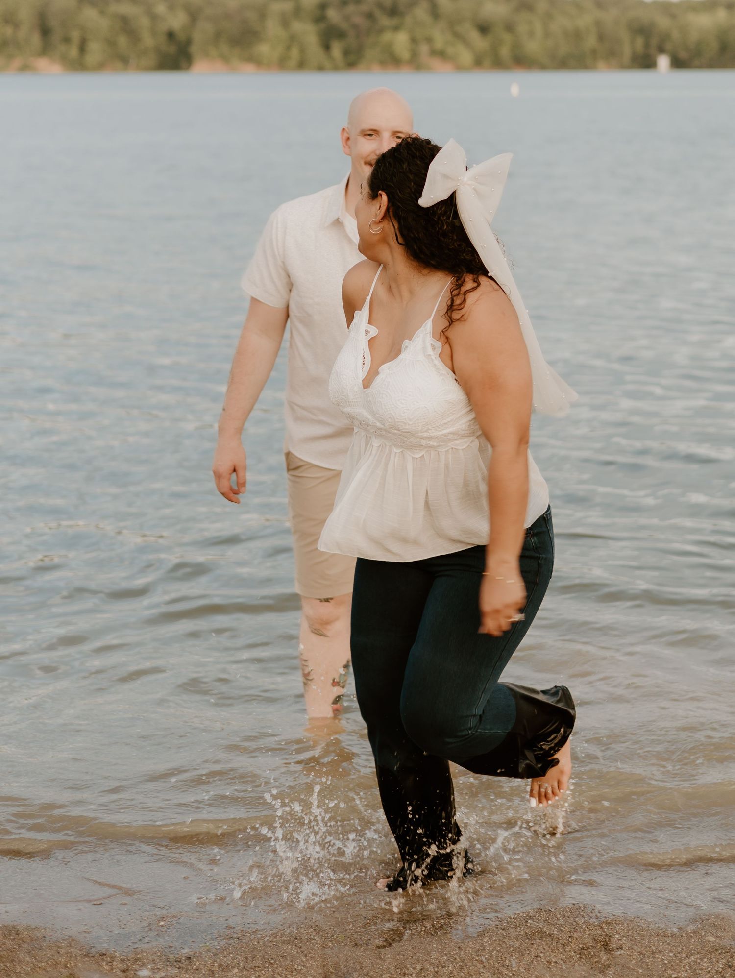 Couple playfully splashing in shallow water at the beach during a romantic photoshoot.