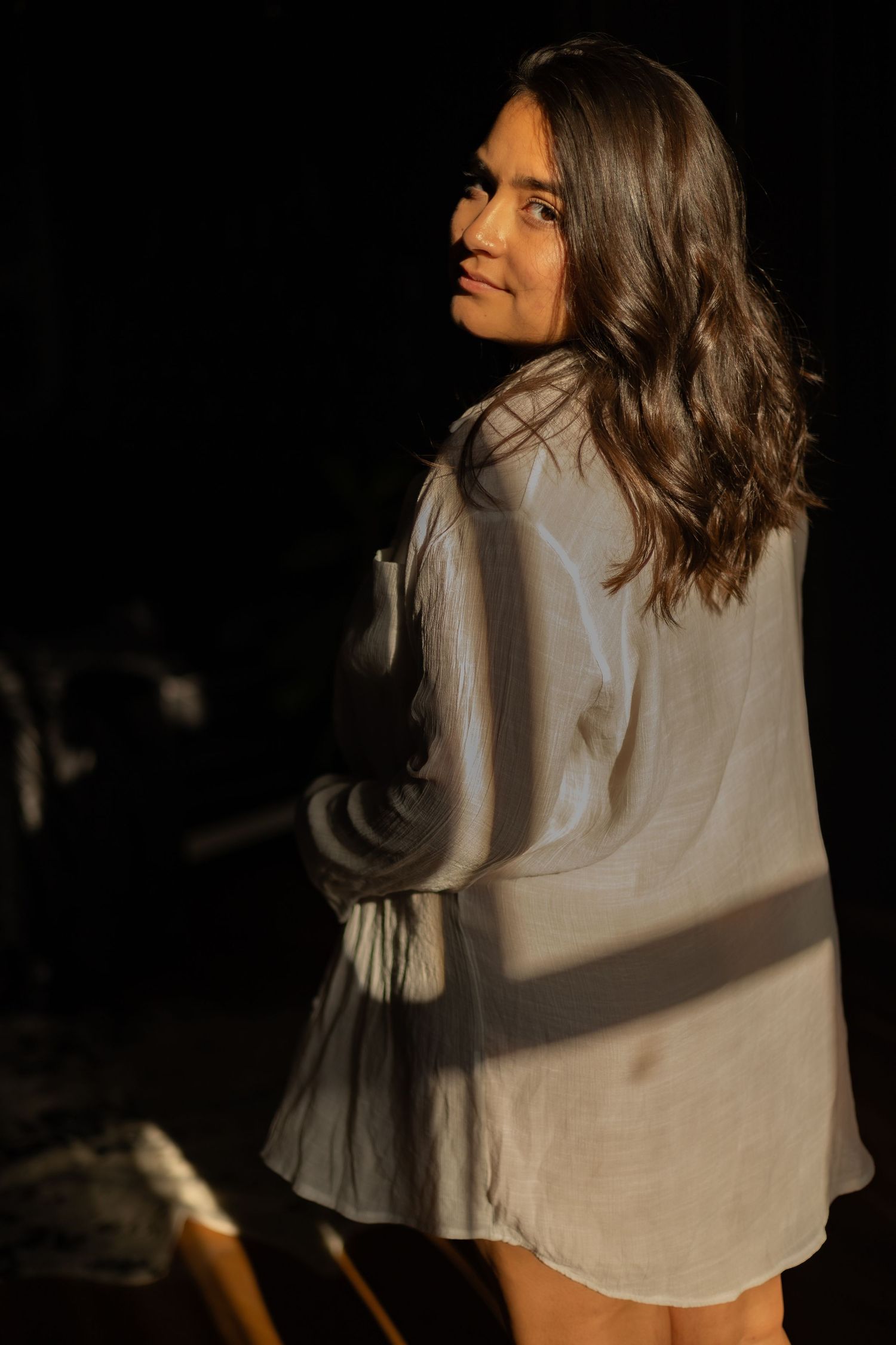 Woman in white dress looking over shoulder with warm lighting against dark background.