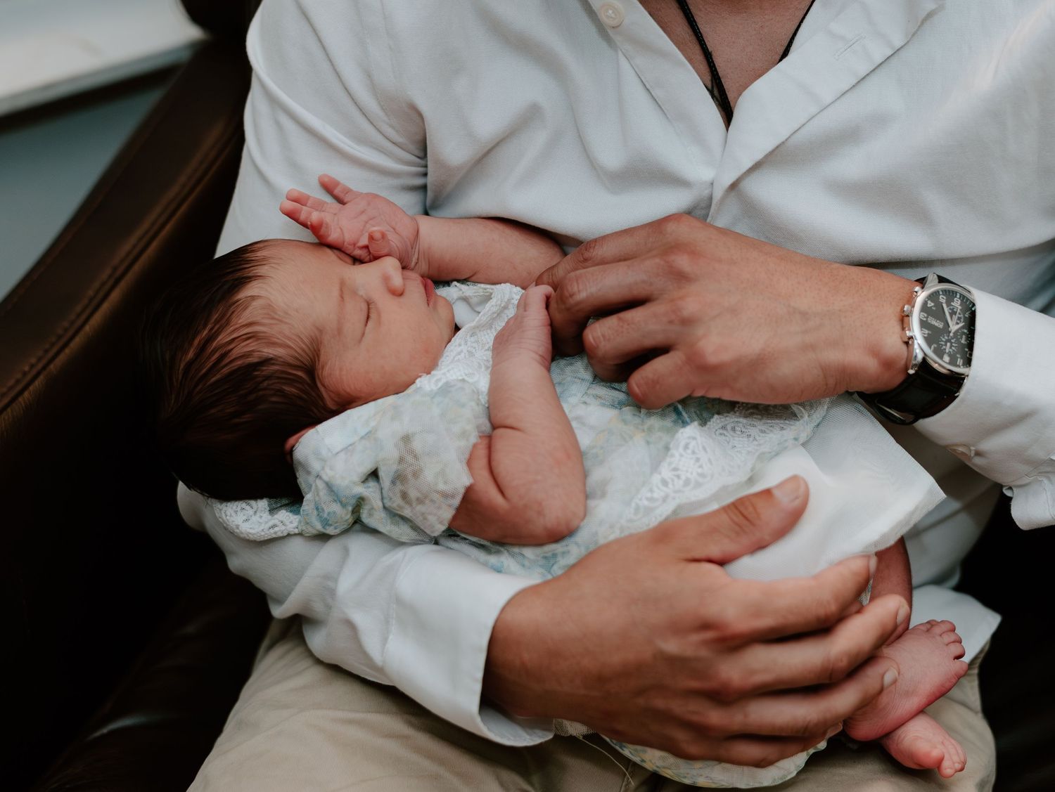 Gentle hands holding a newborn baby wrapped in white clothing.