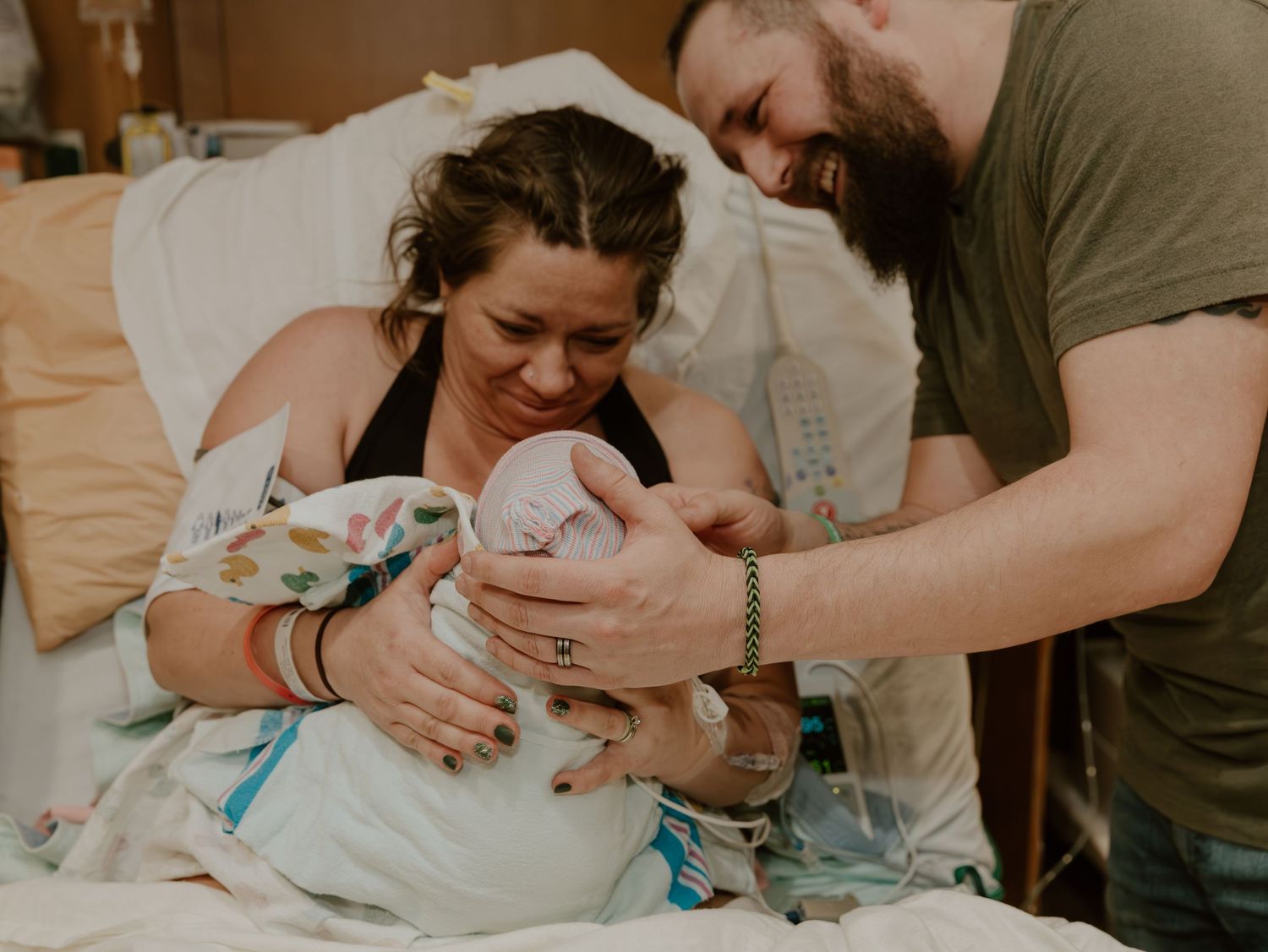 Two parents share a tender moment with their newborn baby in a hospital bed after childbirth.