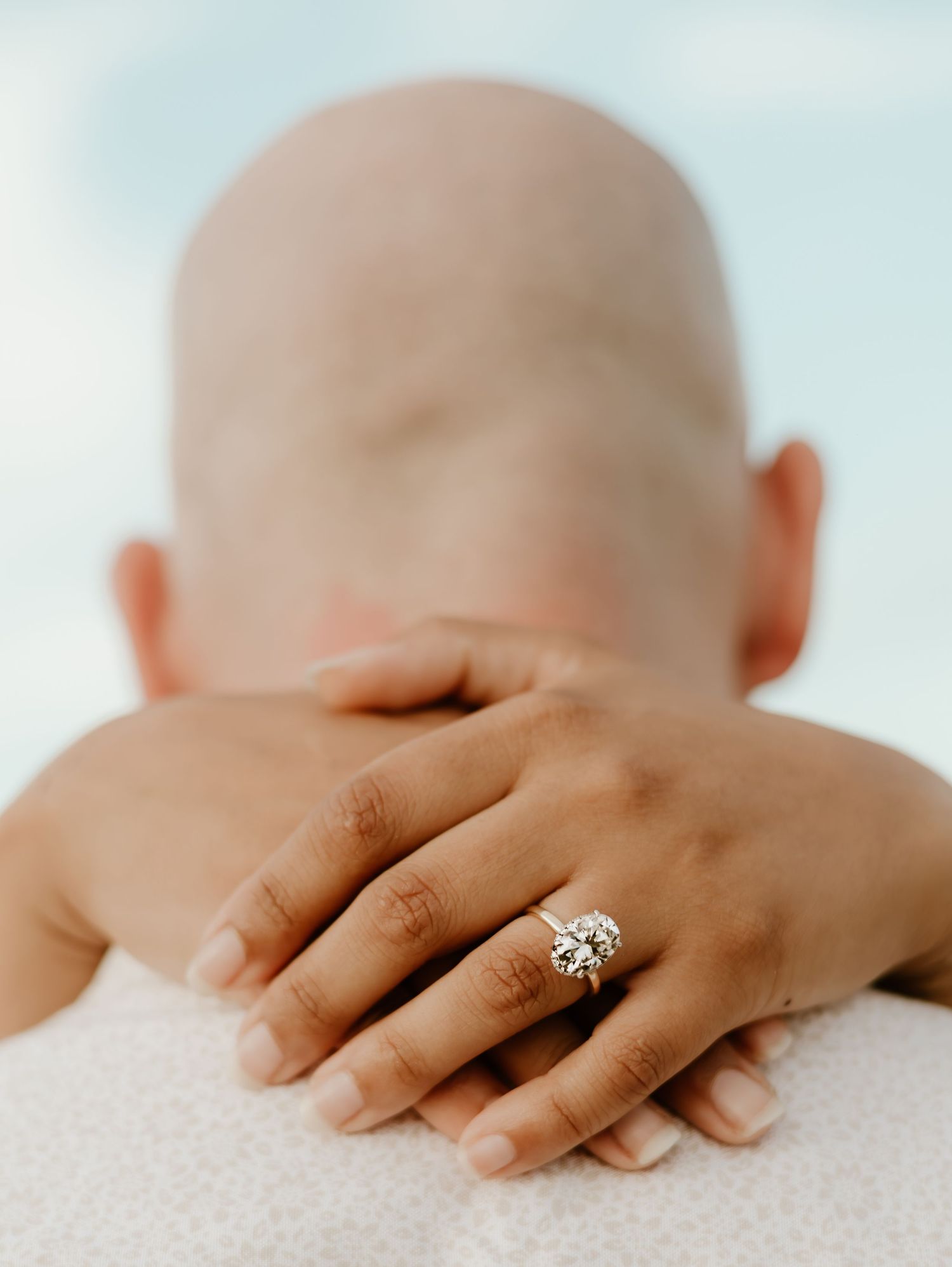 Close-up shot of a hand wearing an engagement ring resting on a light surface.