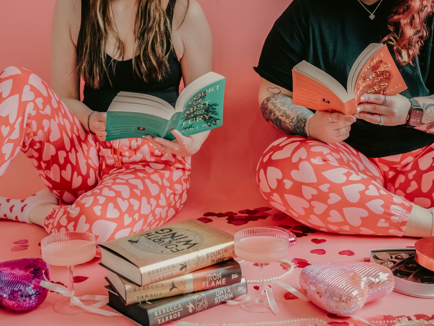 Two readers in matching pajamas relax with books and snacks on a pink background.