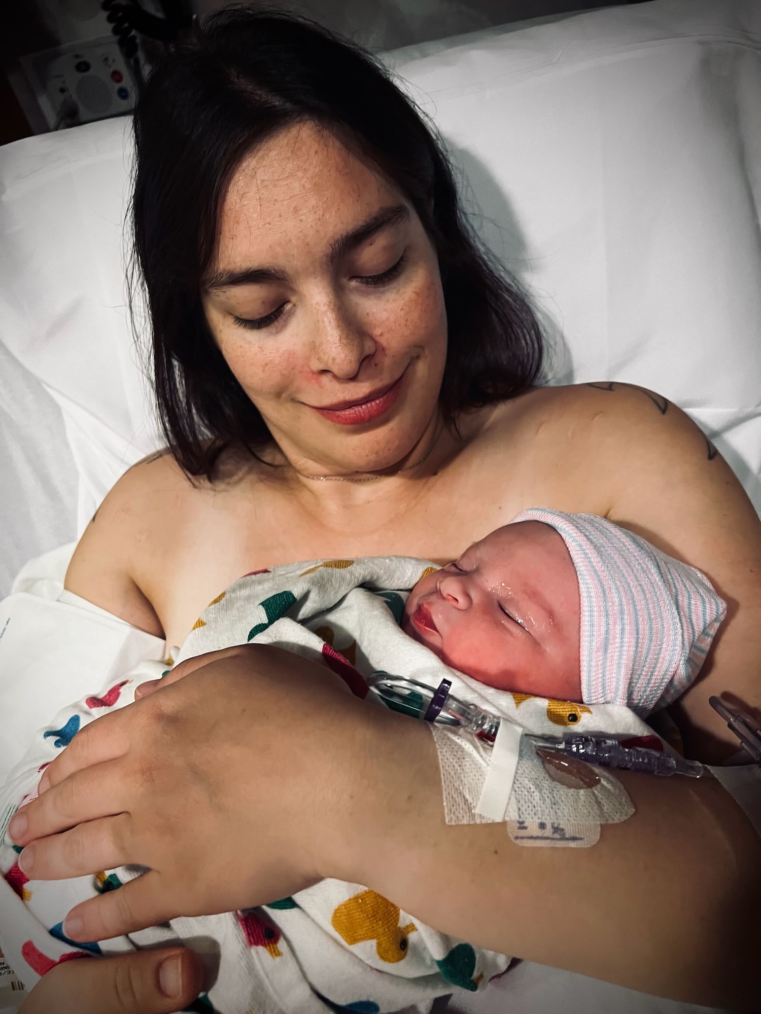 A peaceful moment of skin-to-skin contact between parent and newborn in a hospital bed.