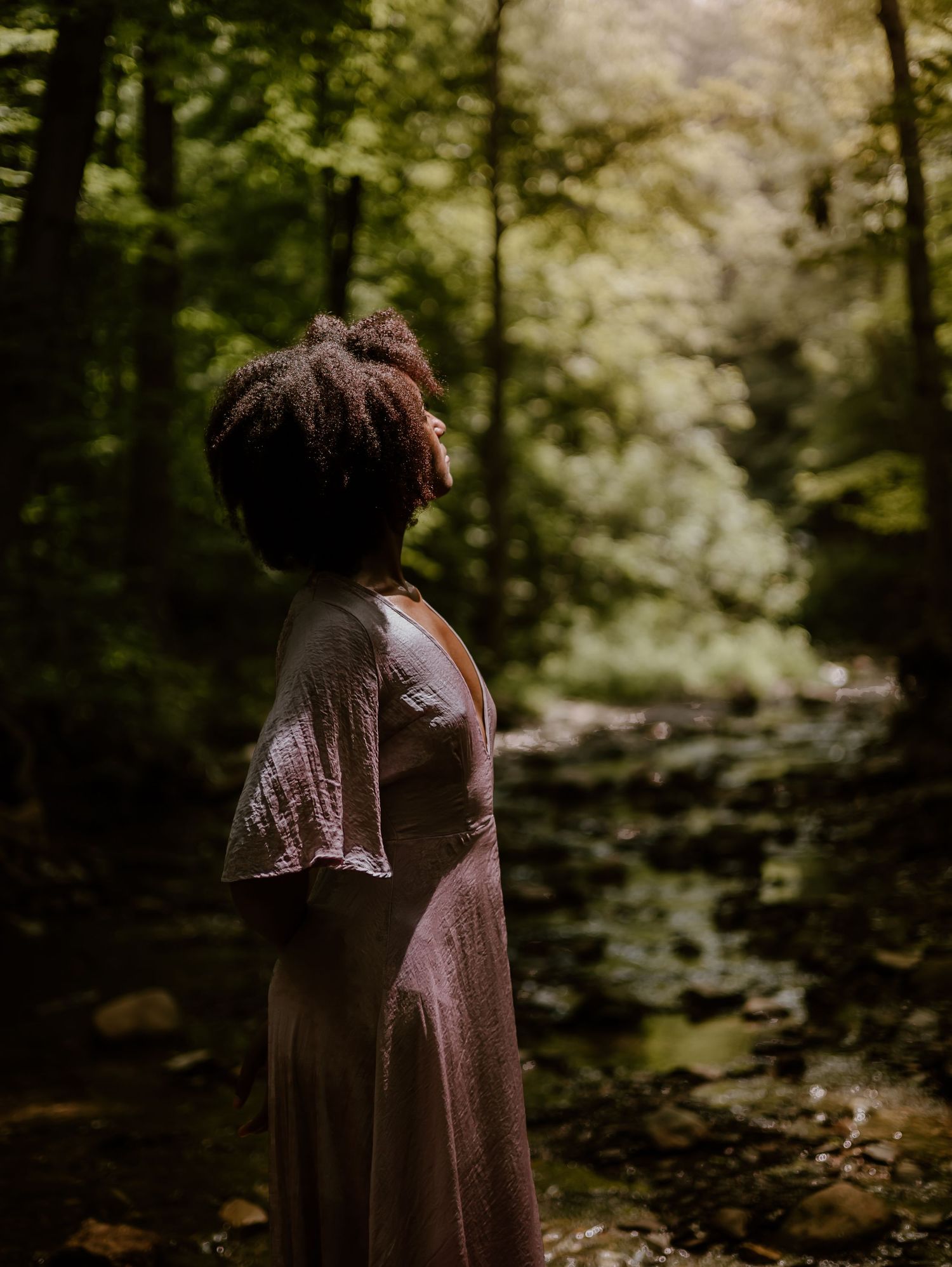 Person stands in a dreamy forest setting wearing vintage-style brown dress amid flowering dogwood trees.