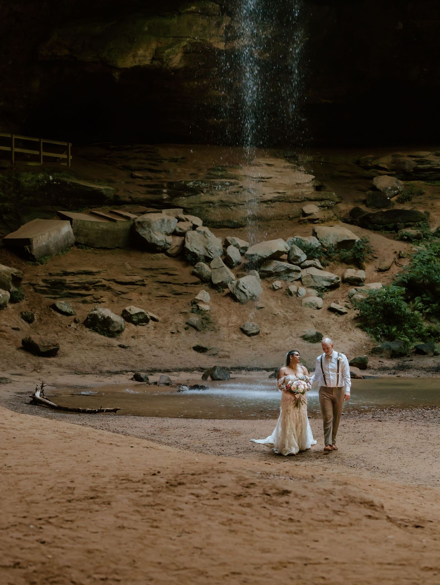 Couple standing together in a rustic cave setting with natural light streaming down through an opening above them.