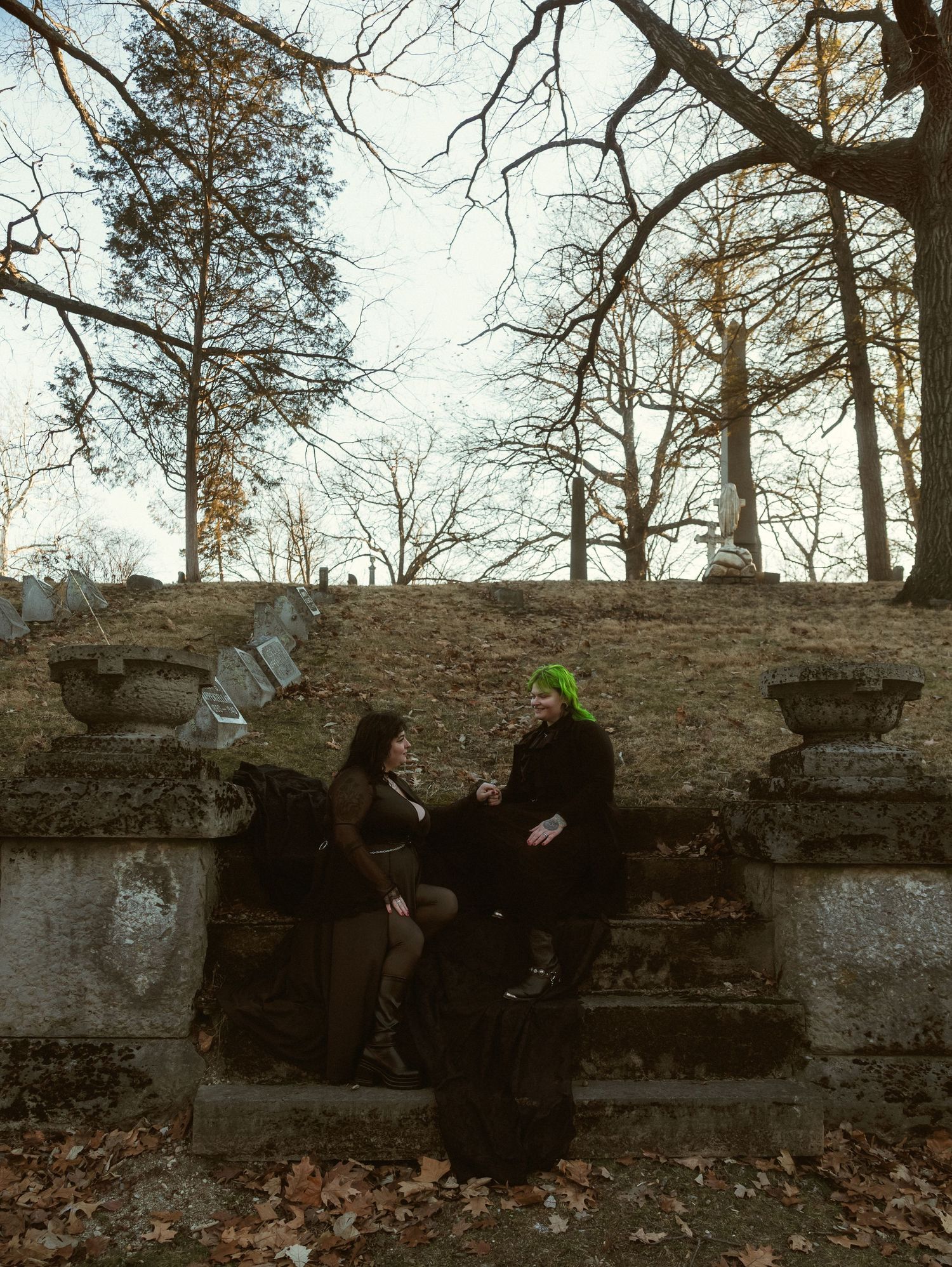 Figures in dark clothing sit along an old stone wall surrounded by bare winter trees.