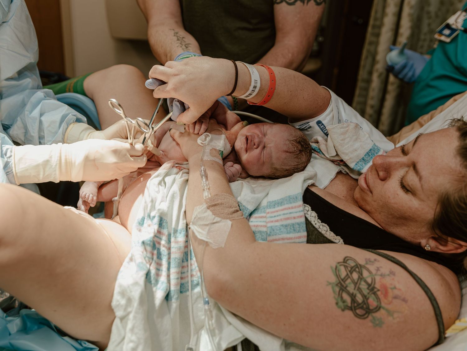 A newborn baby is held up by medical staff moments after birth in a hospital delivery room.