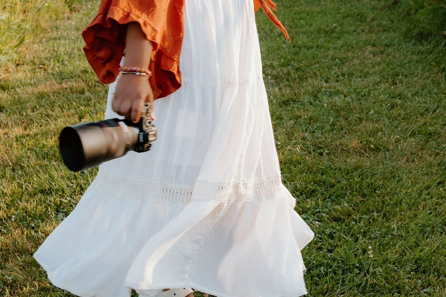 A white flowy dress twirls gracefully against a green grassy background in golden sunlight.