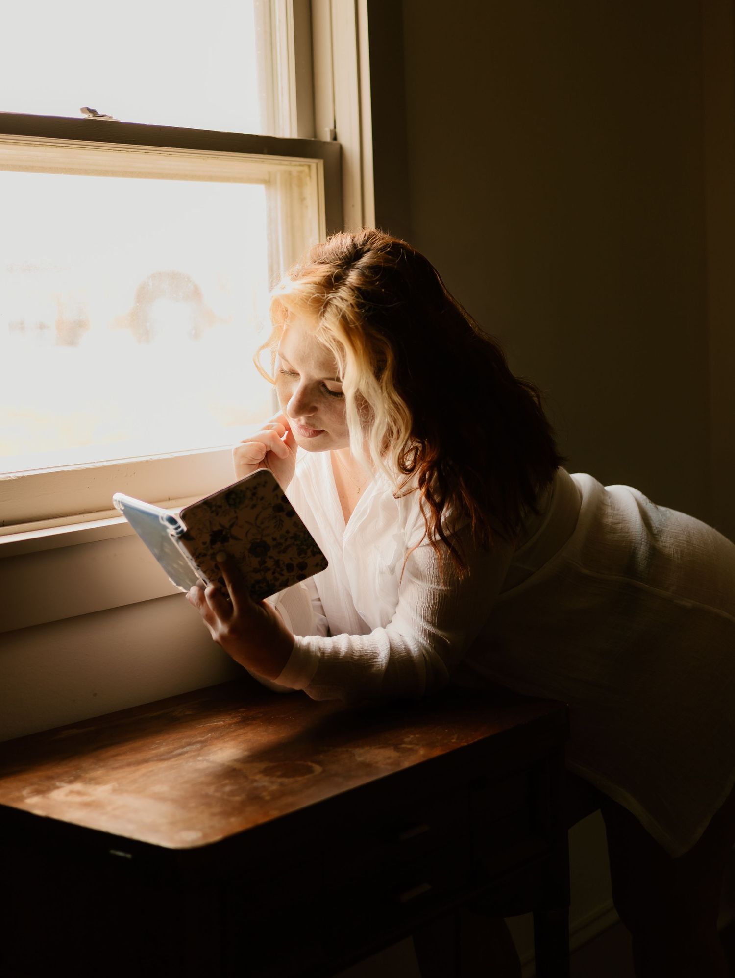 A person in golden sunlight sits at a wooden desk reading a book by a window in a series of connected photos.