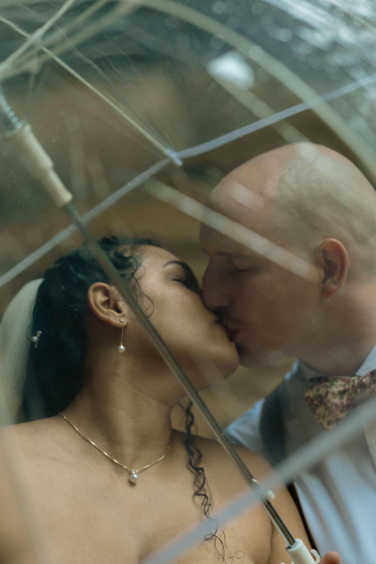 Romantic wedding couple sharing an intimate kiss under a sheer veil in soft lighting.