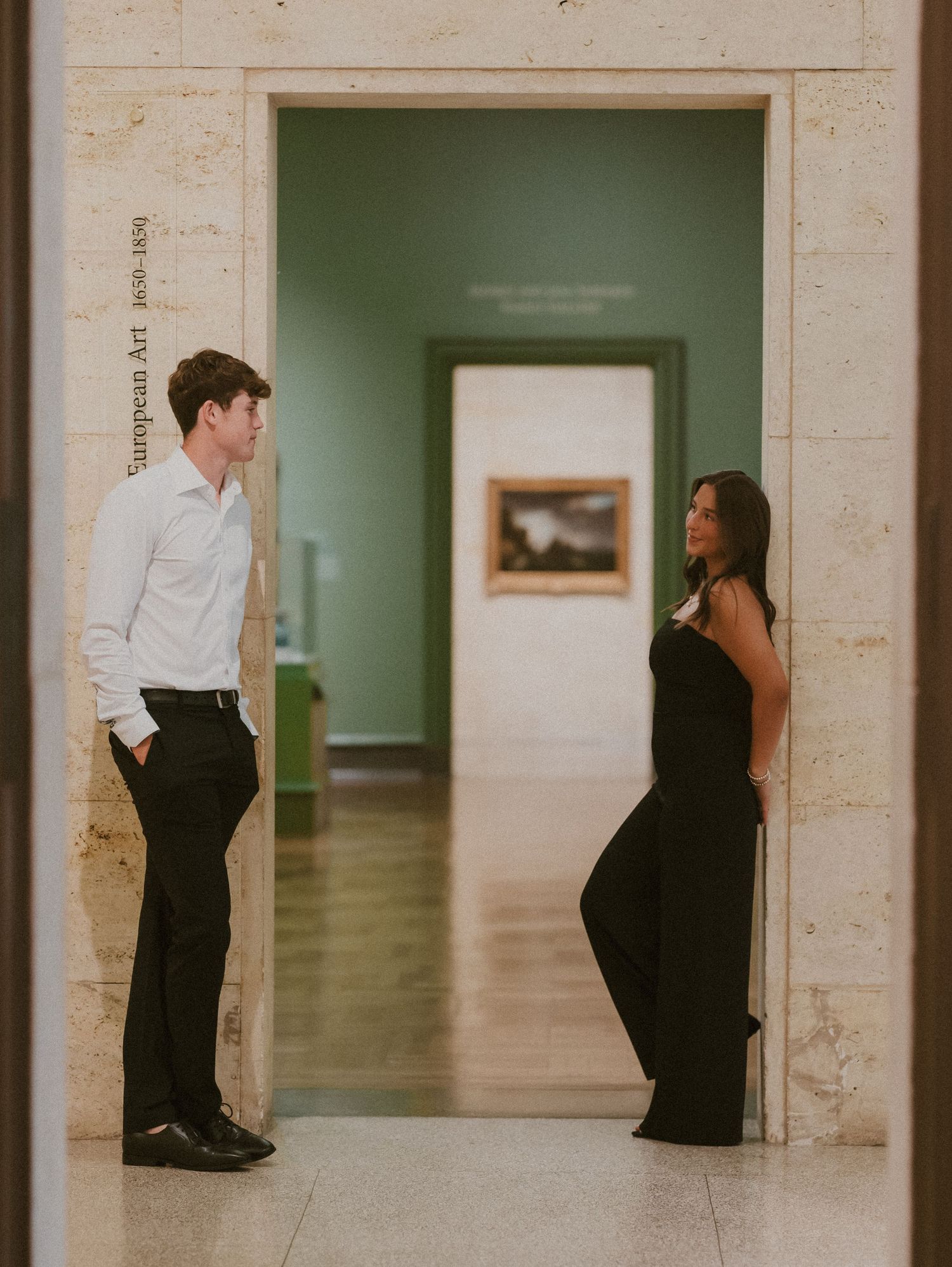 A couple poses playfully in a museum hallway with mint green walls.