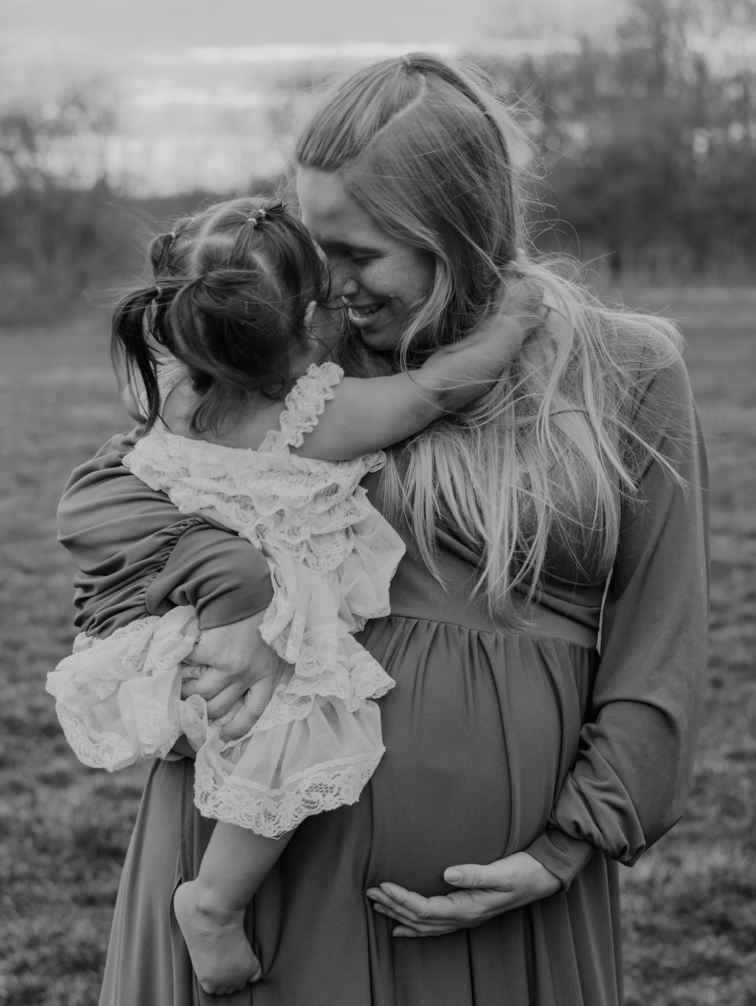 A touching black and white photo of a tender embrace between a parent and child in a long dress, with a visible baby bump.