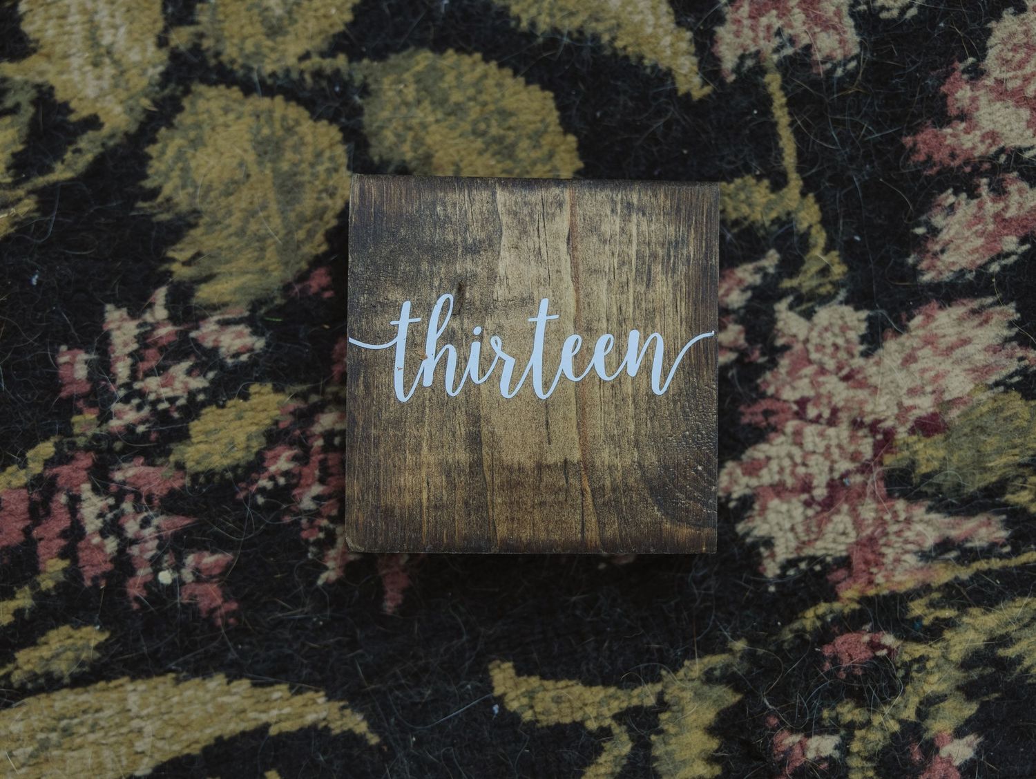 Rustic wooden signs with handwritten text against a dark floral background.