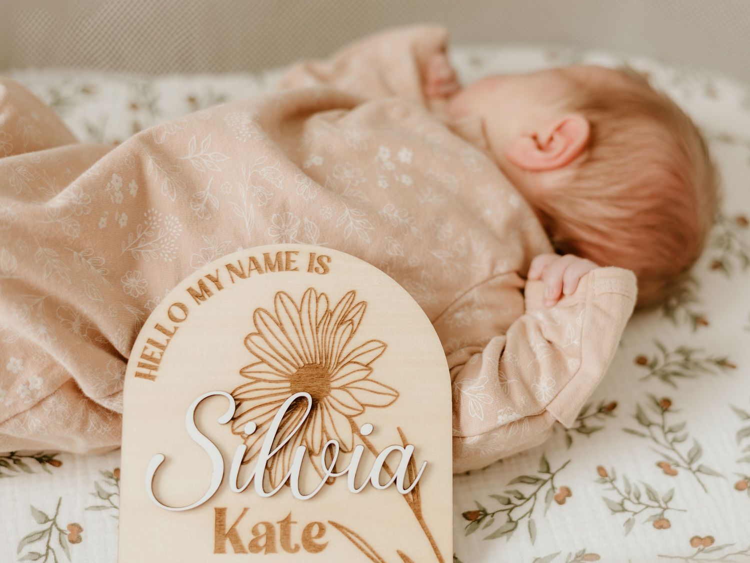 Soft peach-toned newborn photography details with a wooden name plaque featuring floral design.