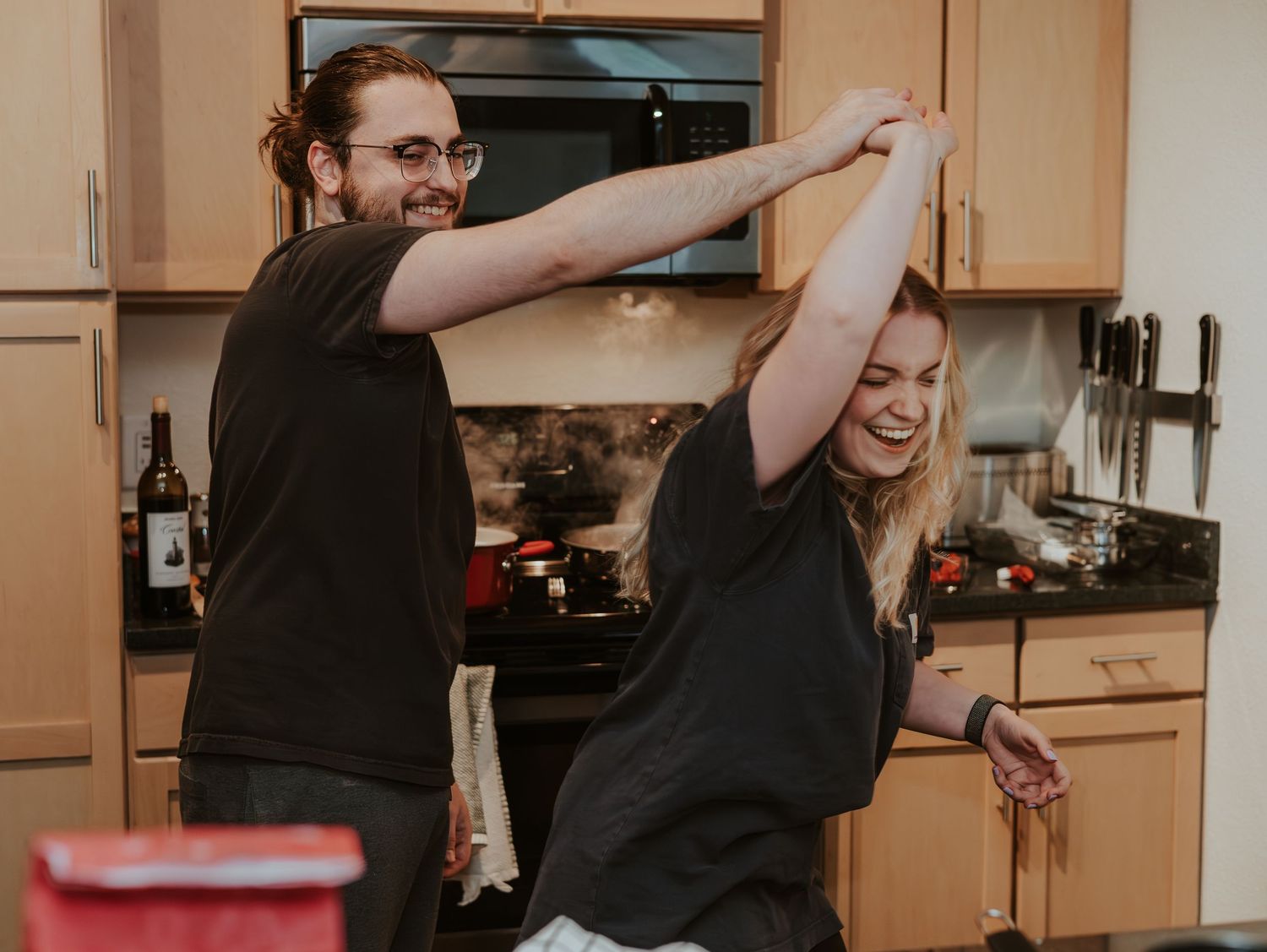 A group of people in a kitchen perform synchronized dabbing dance moves while wearing black shirts.