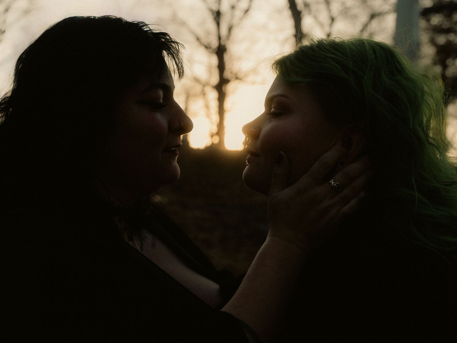 A couple shares a romantic kiss in a garden during sunset with warm golden light filtering through trees.