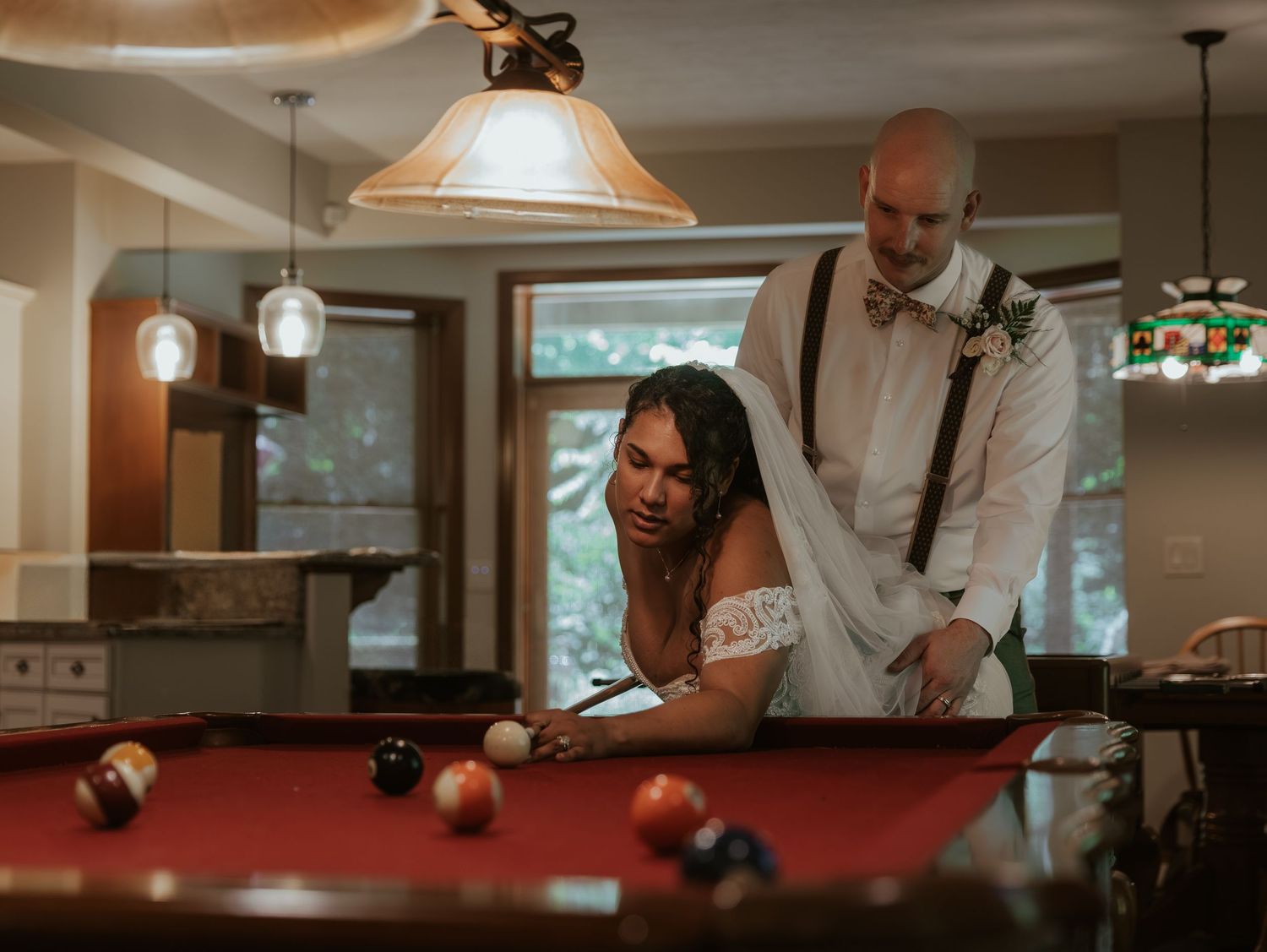 Couple enjoying a playful moment at a pool table in a warmly lit room.
