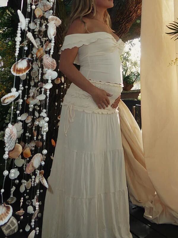 Off-shoulder white tiered maxi dress shown next to a decorated Christmas tree with seashell ornaments.
