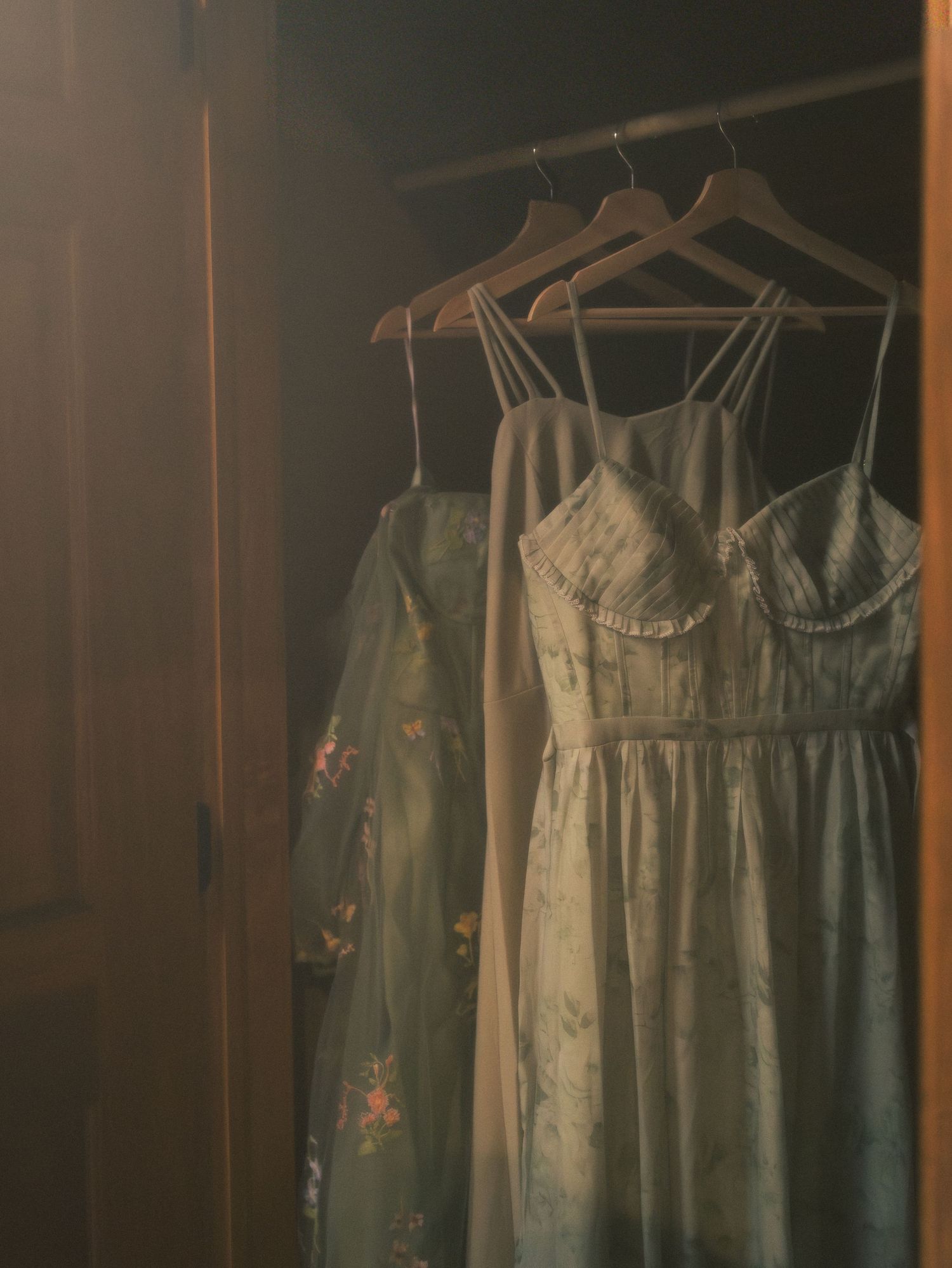 Pastel bridesmaid dresses hanging in a dimly lit dressing room before the ceremony.