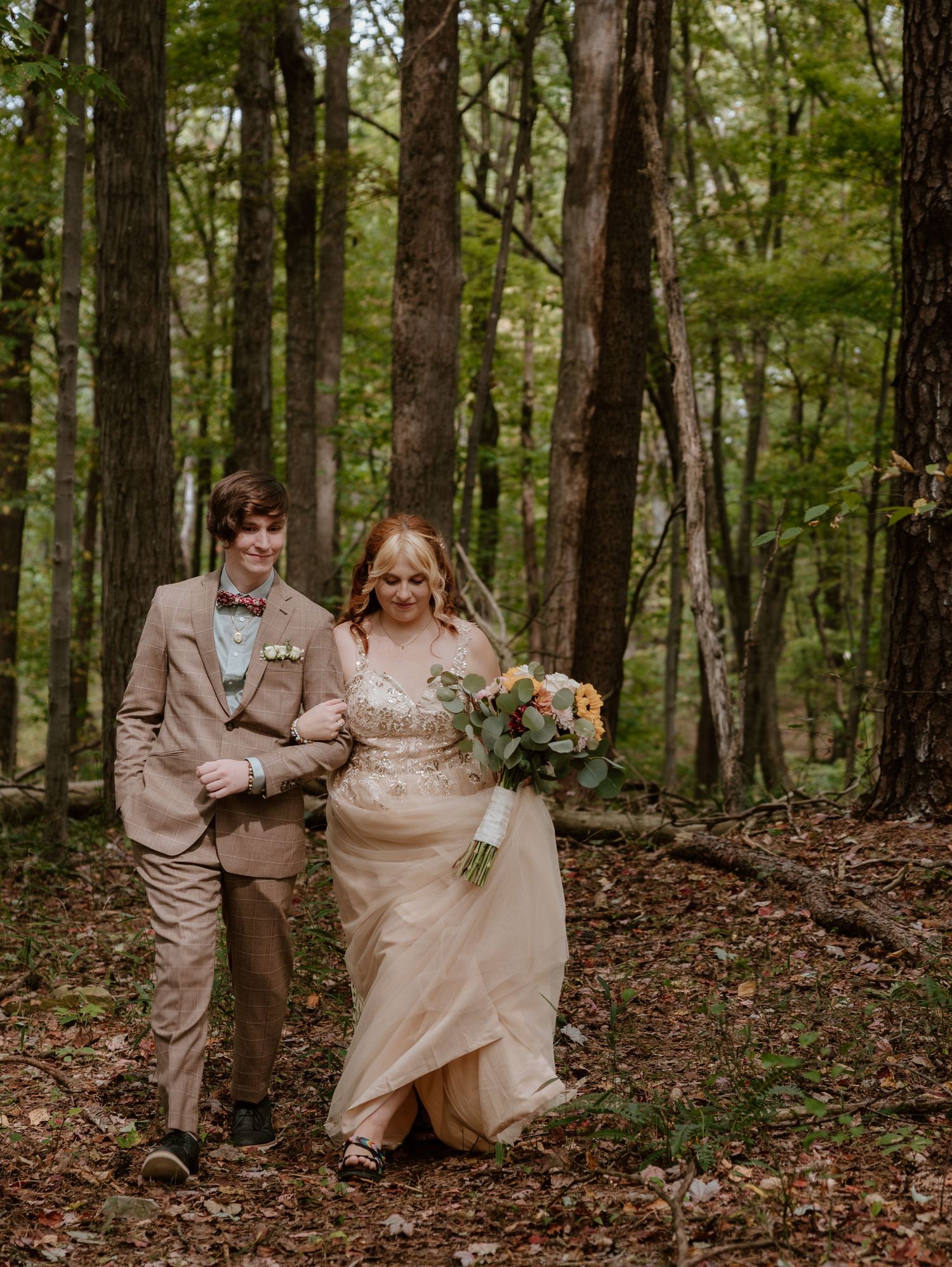Couple walking through autumn forest in champagne wedding dress and tan suit.