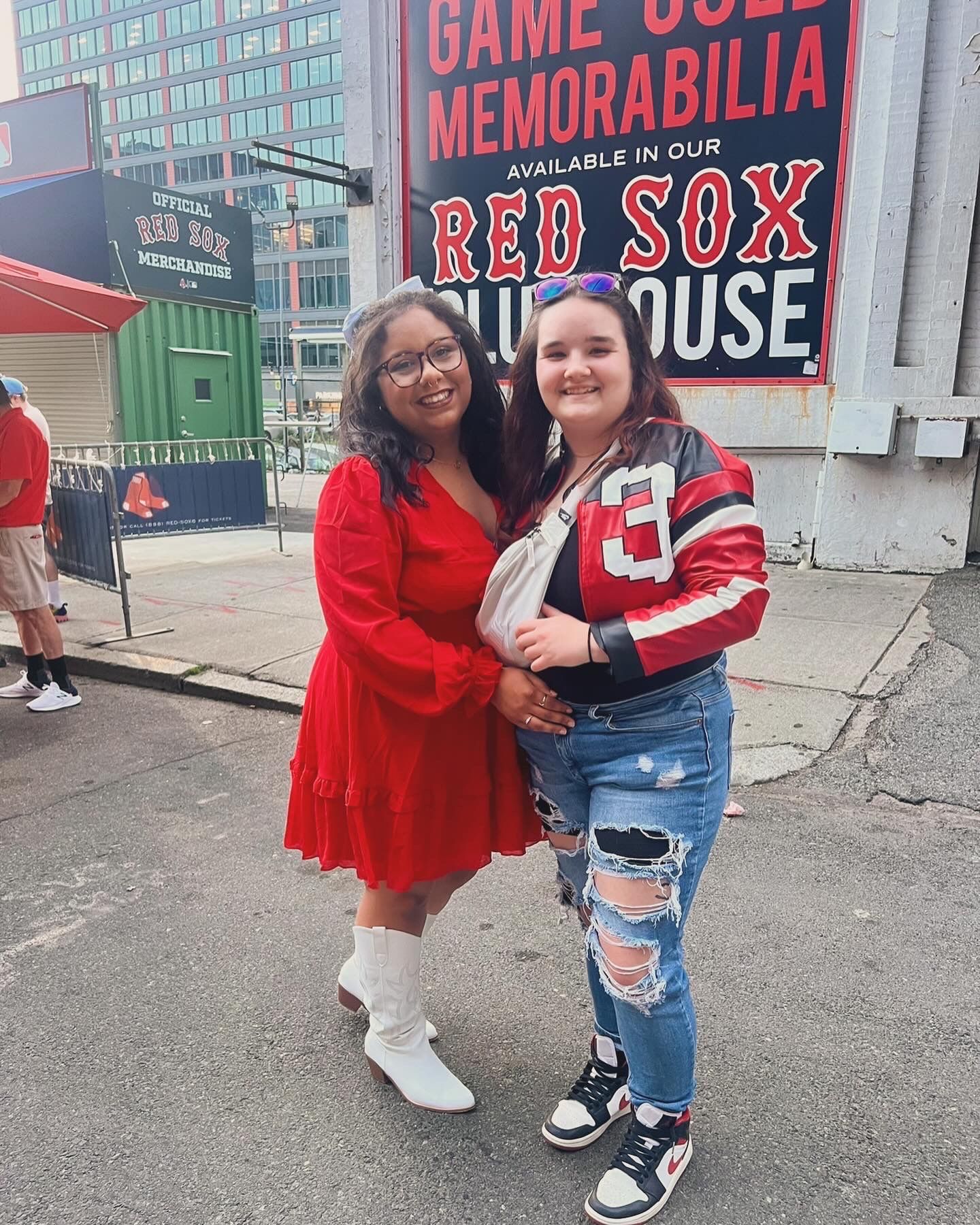 Two friends posing together outside Fenway Park with Red Sox memorabilia signage visible.