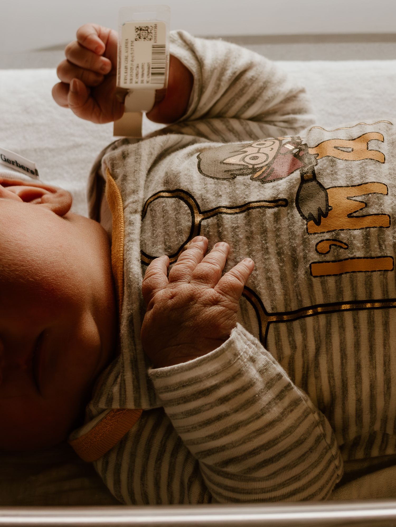 A baby wearing striped clothing lies on a cushioned surface while reading a book with illustrated characters.
