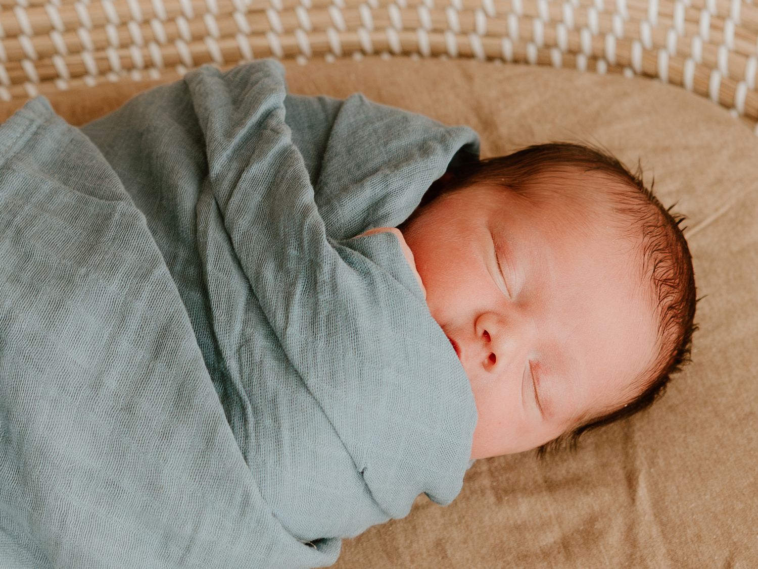 Newborn baby in grey clothing sleeping peacefully in a woven basket.