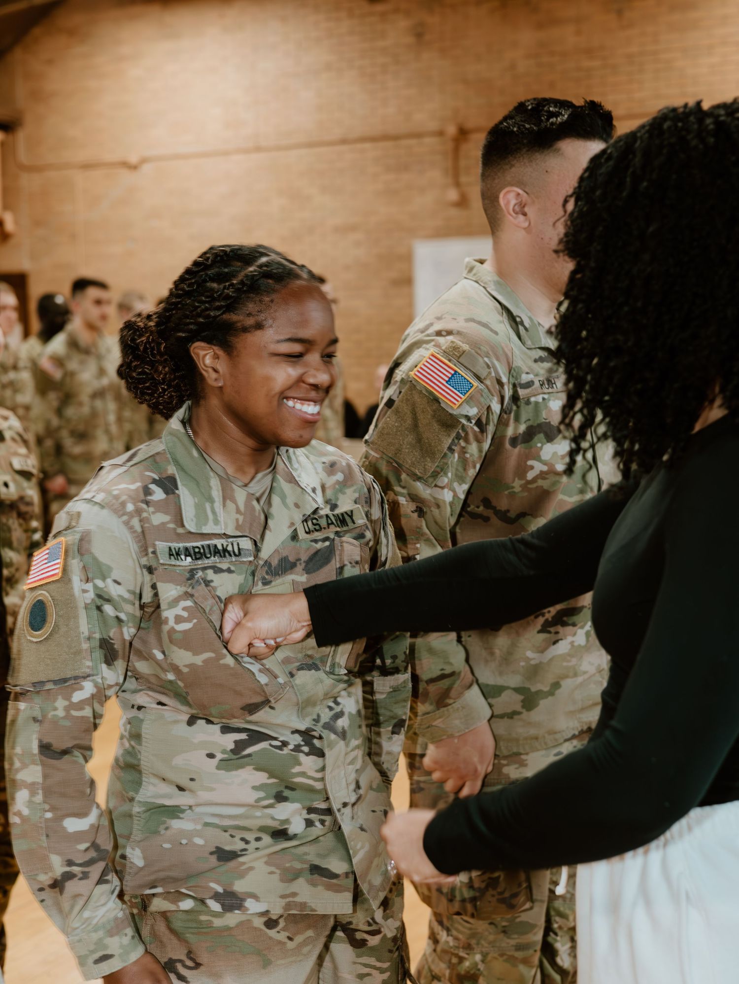 Military service member in camouflage uniform shares a joyful moment during what appears to be a ceremony.