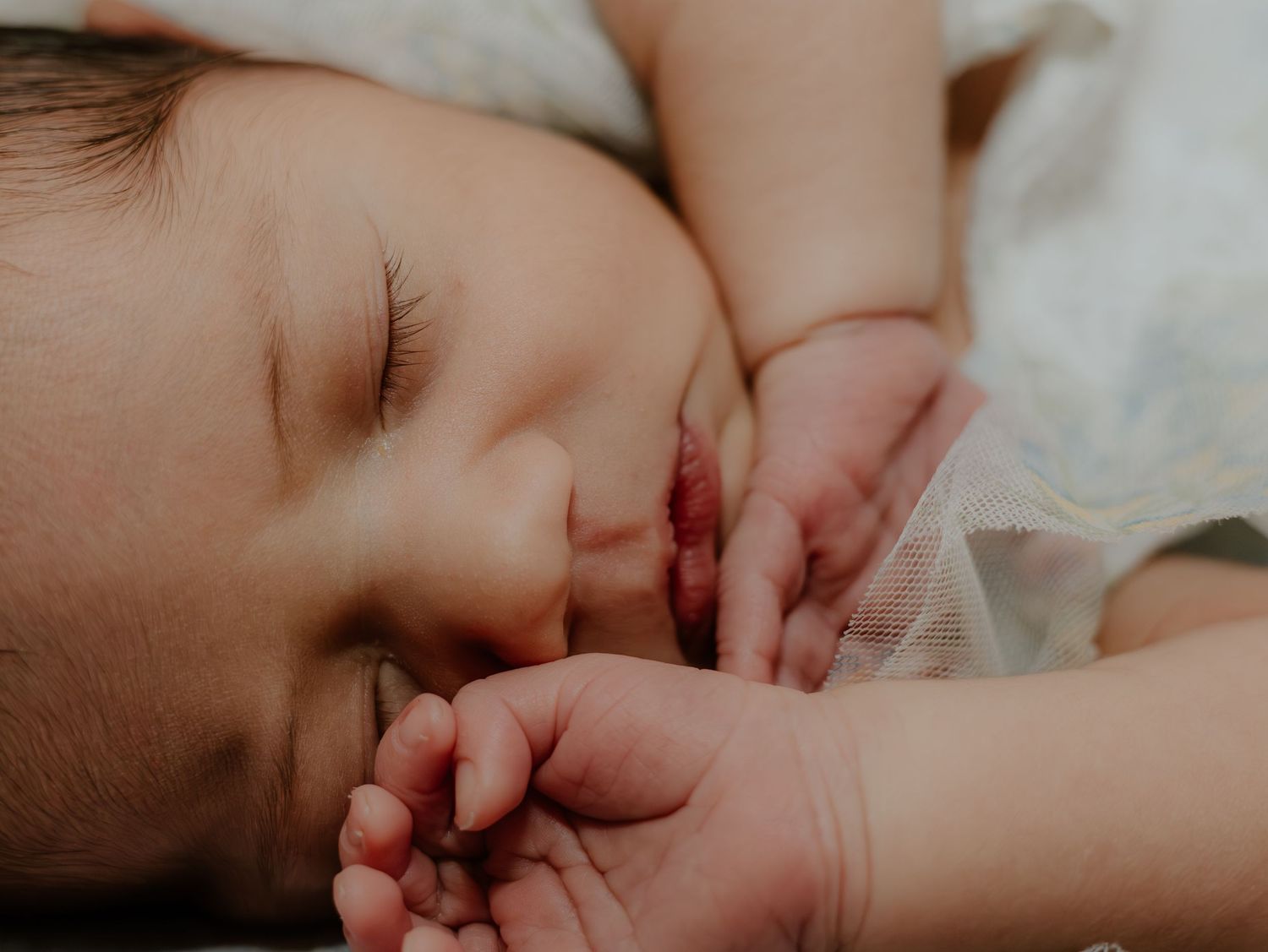 A sleeping baby peacefully rests against soft white bedding in a series of gentle close-up shots.