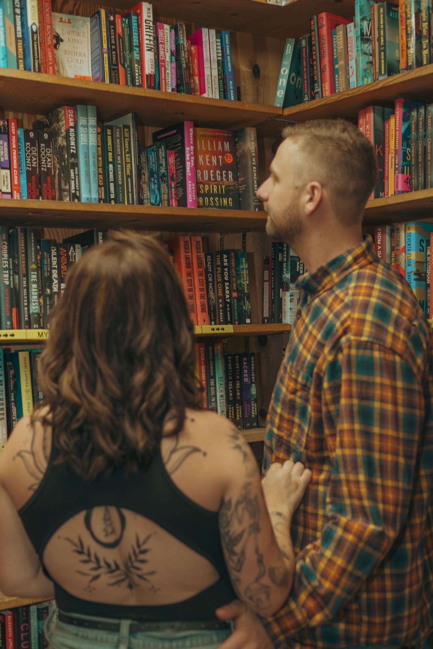 A couple browses books together in a cozy library with wooden shelves filled with colorful book spines.