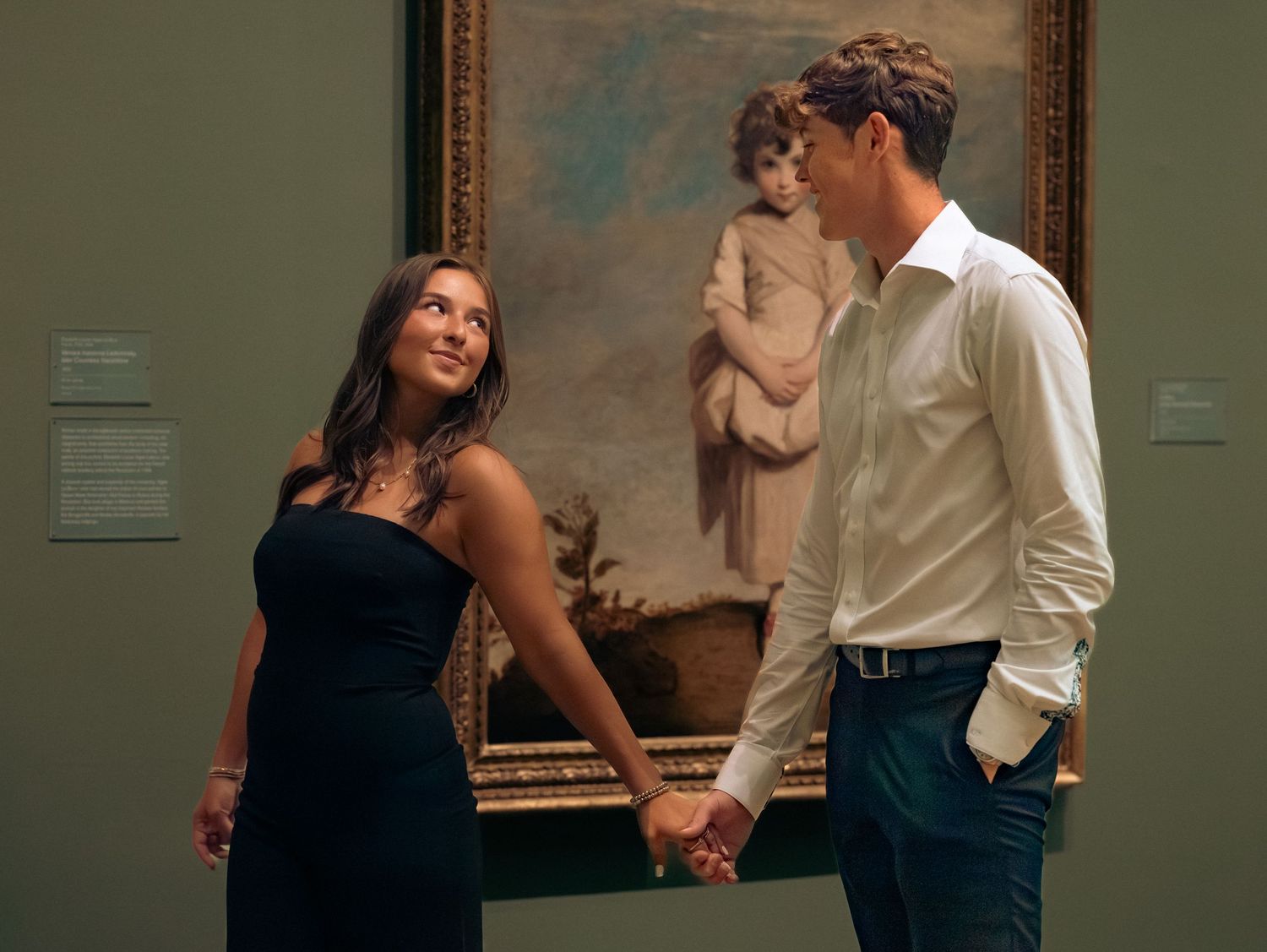 A romantic couple in formal attire embraces intimately against a green wall in an elegant setting.