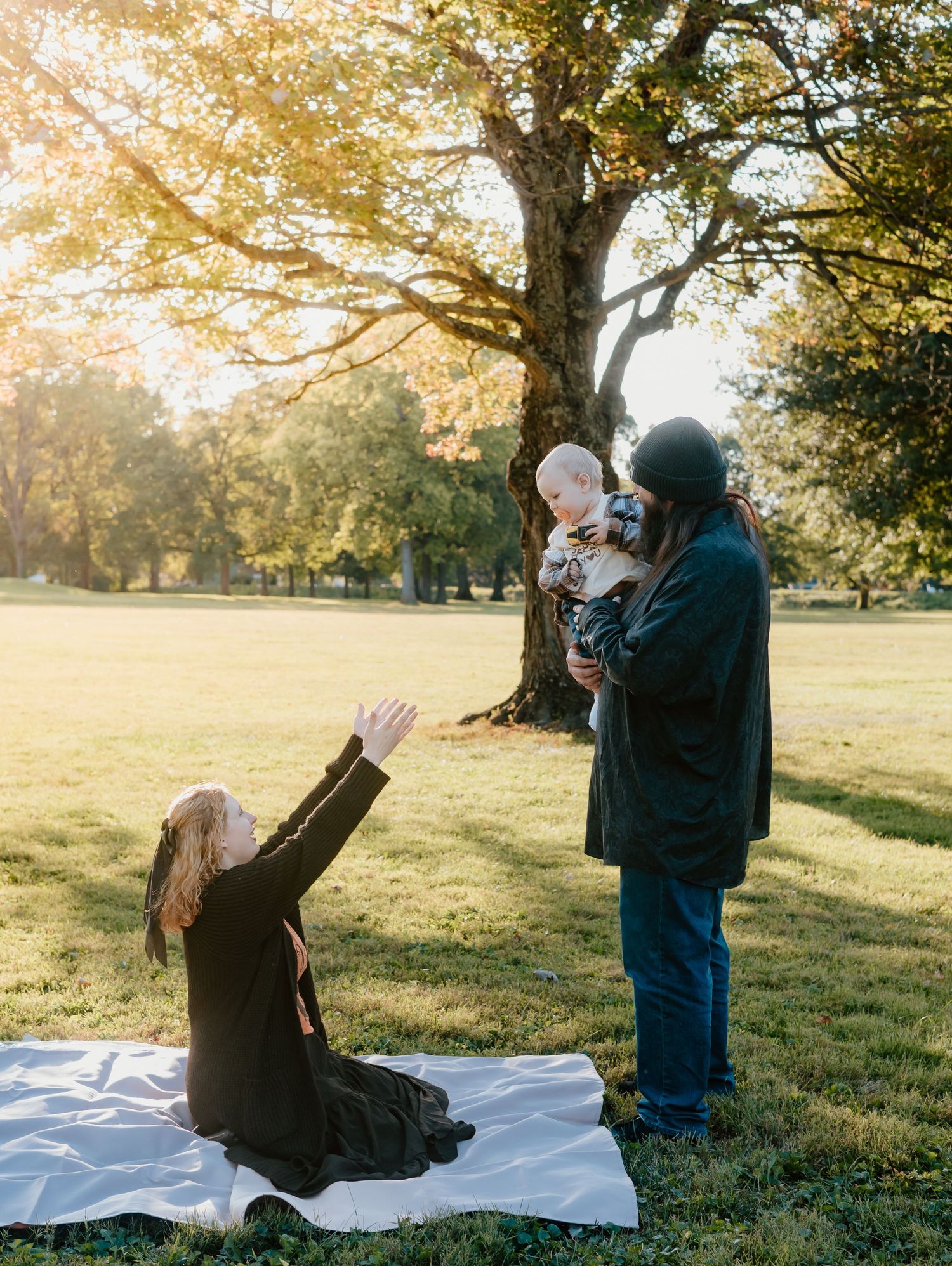A couple enjoys a playful moment on a blanket in a sunlit park during autumn.