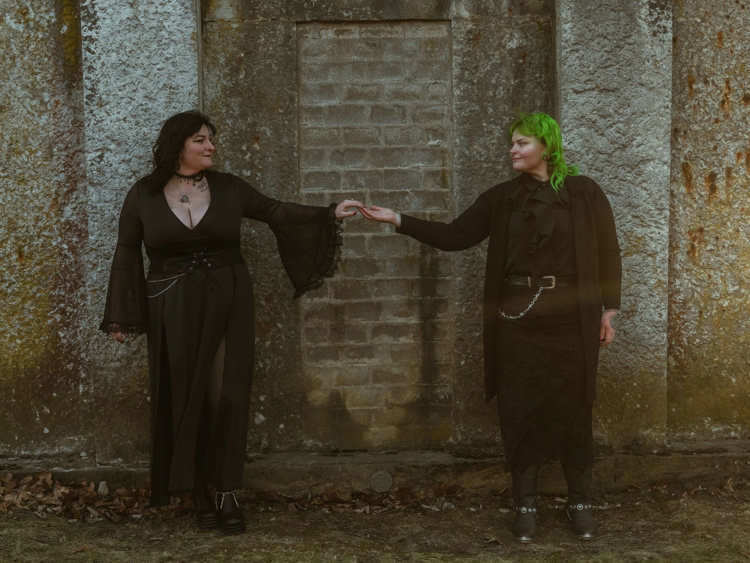 People standing against a weathered stone wall in dark clothing.