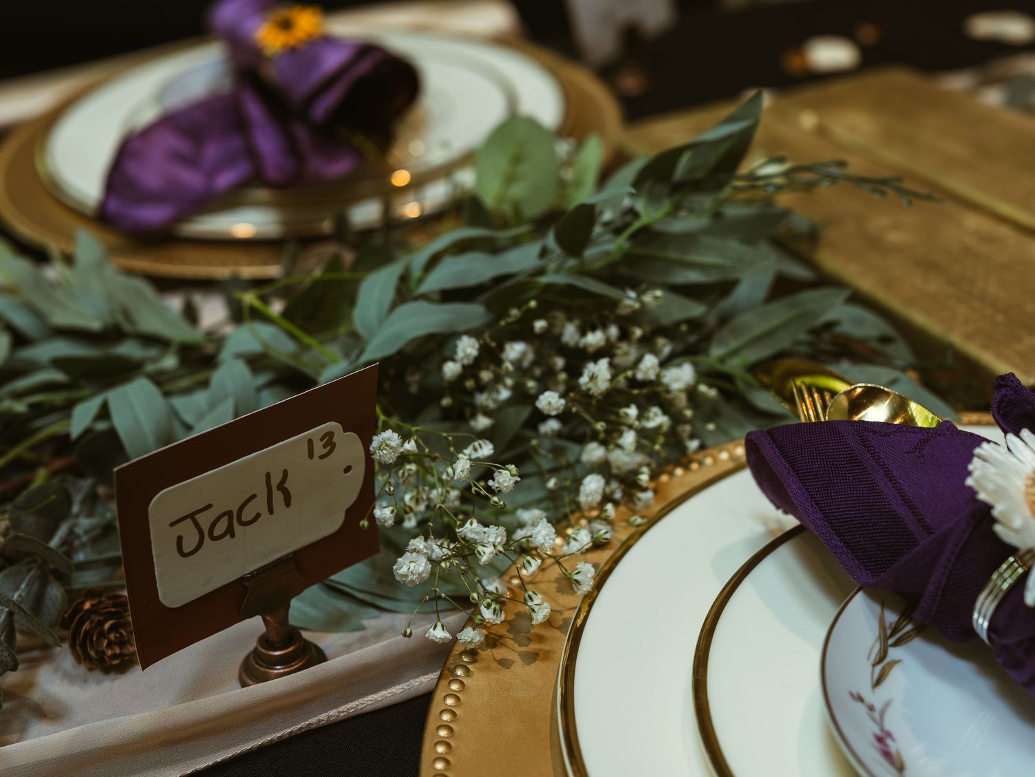 Wedding reception table decorated with purple flowers, greenery, and place cards in rustic style.