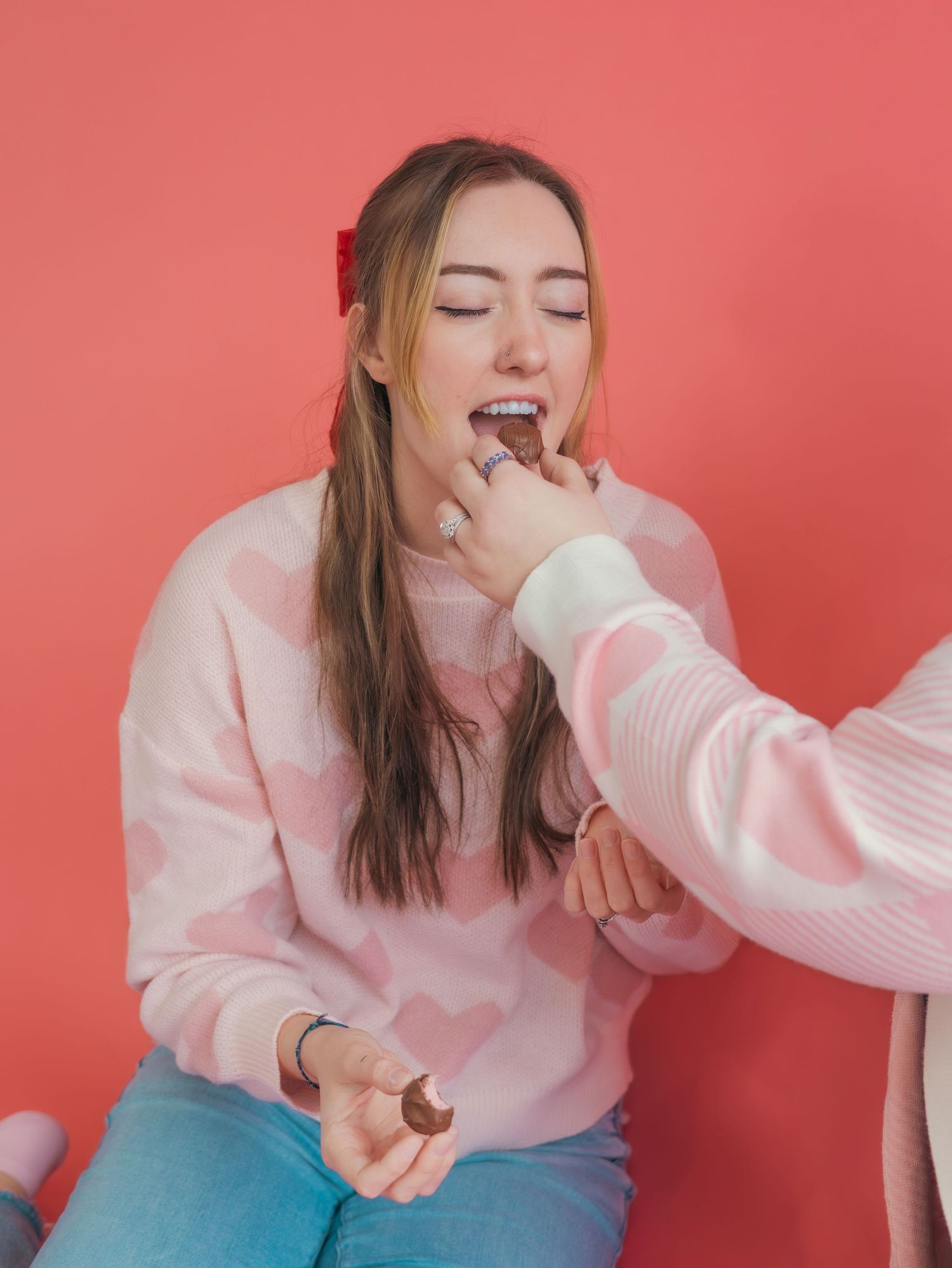 Someone in a pink sweater enjoying chocolate against a coral background.