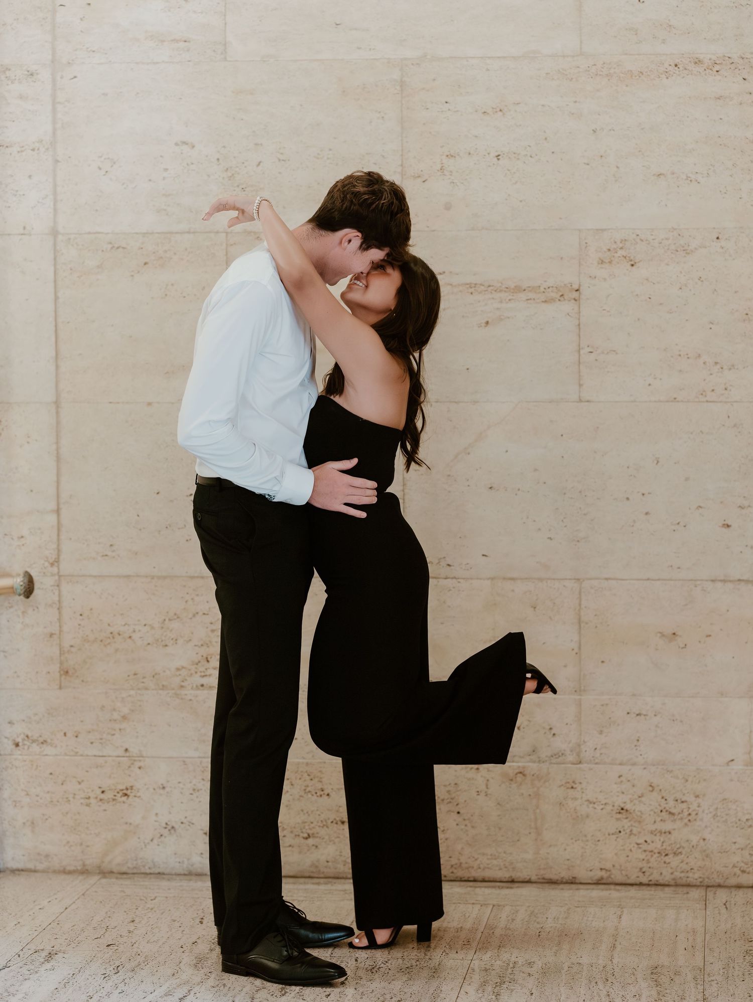 A romantic couple dancing together in front of a beige wall, captured in a series of intimate poses.