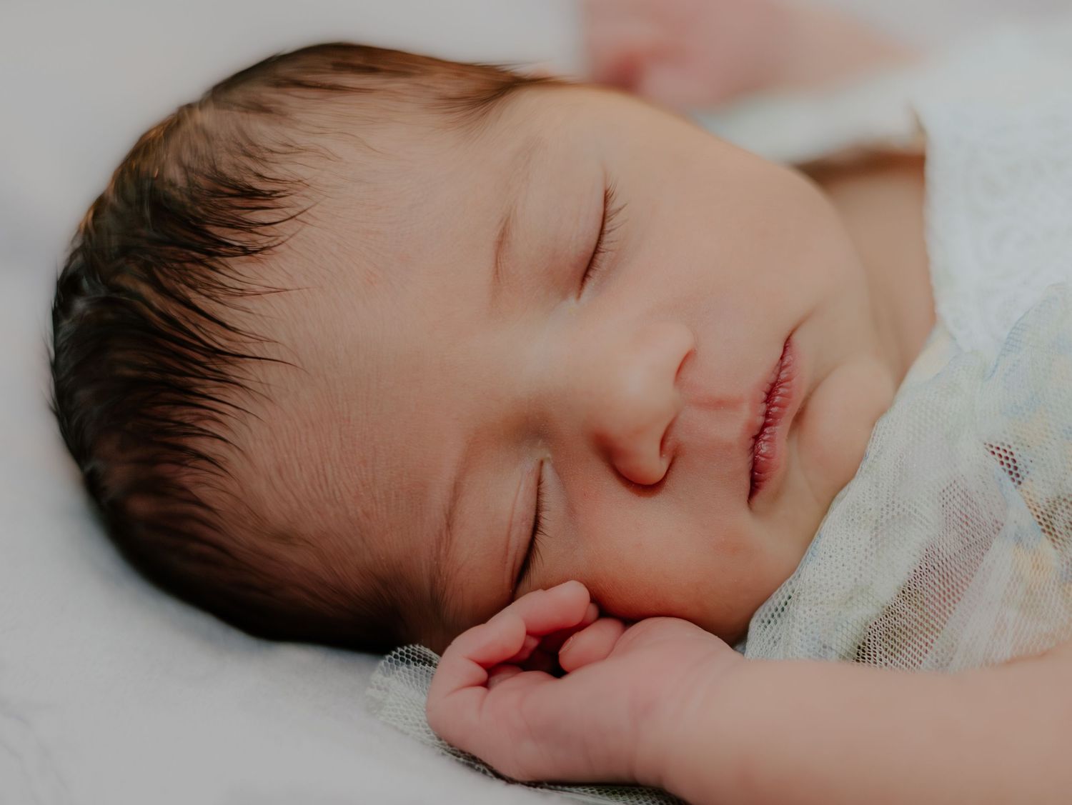 A sleeping newborn baby rests peacefully on white bedding in a series of tender close-up shots.